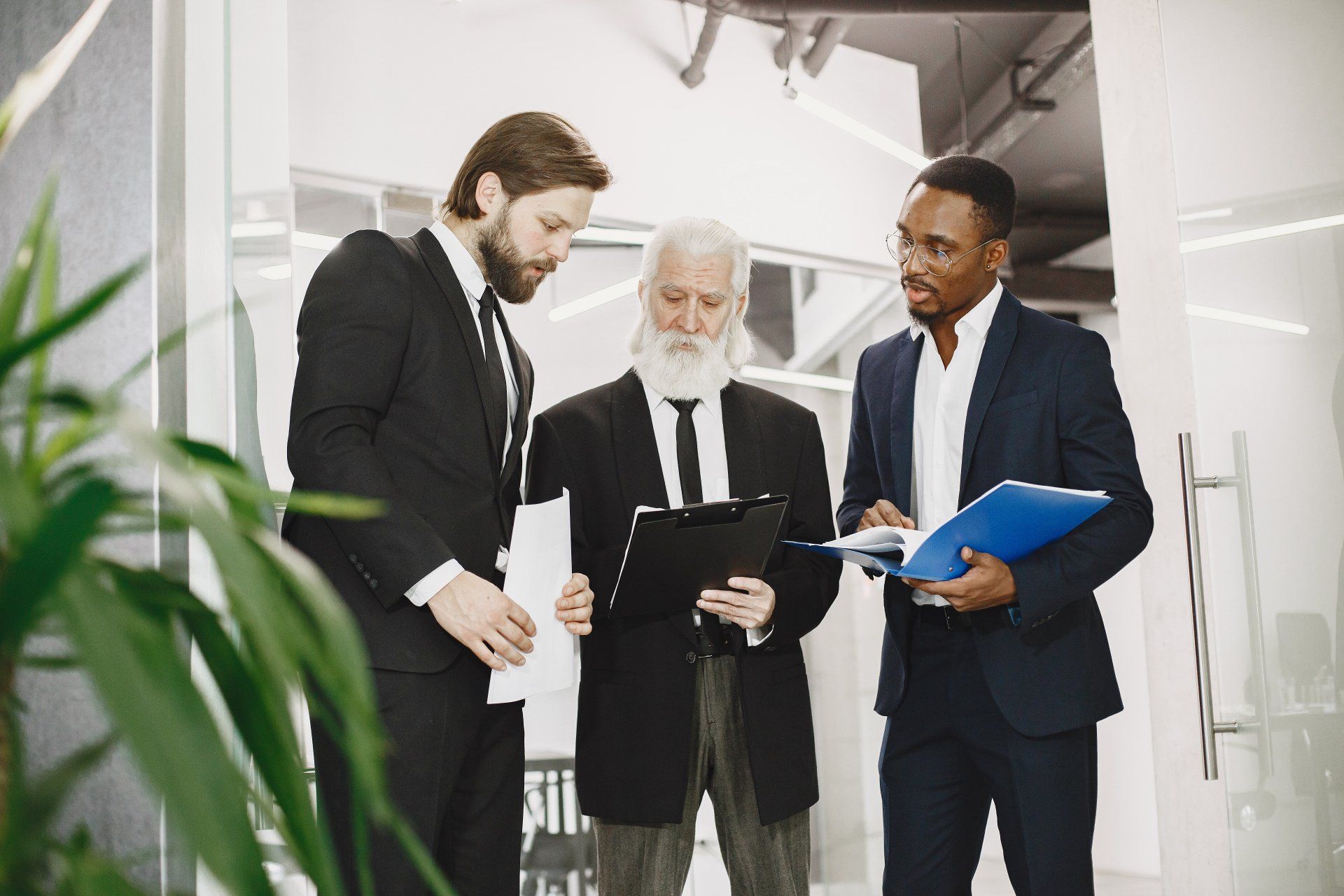 Three men in suits are standing next to each other in an office looking at a clipboard.