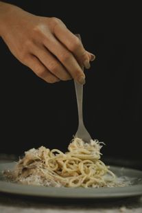 A person is holding a fork over a plate of spaghetti.