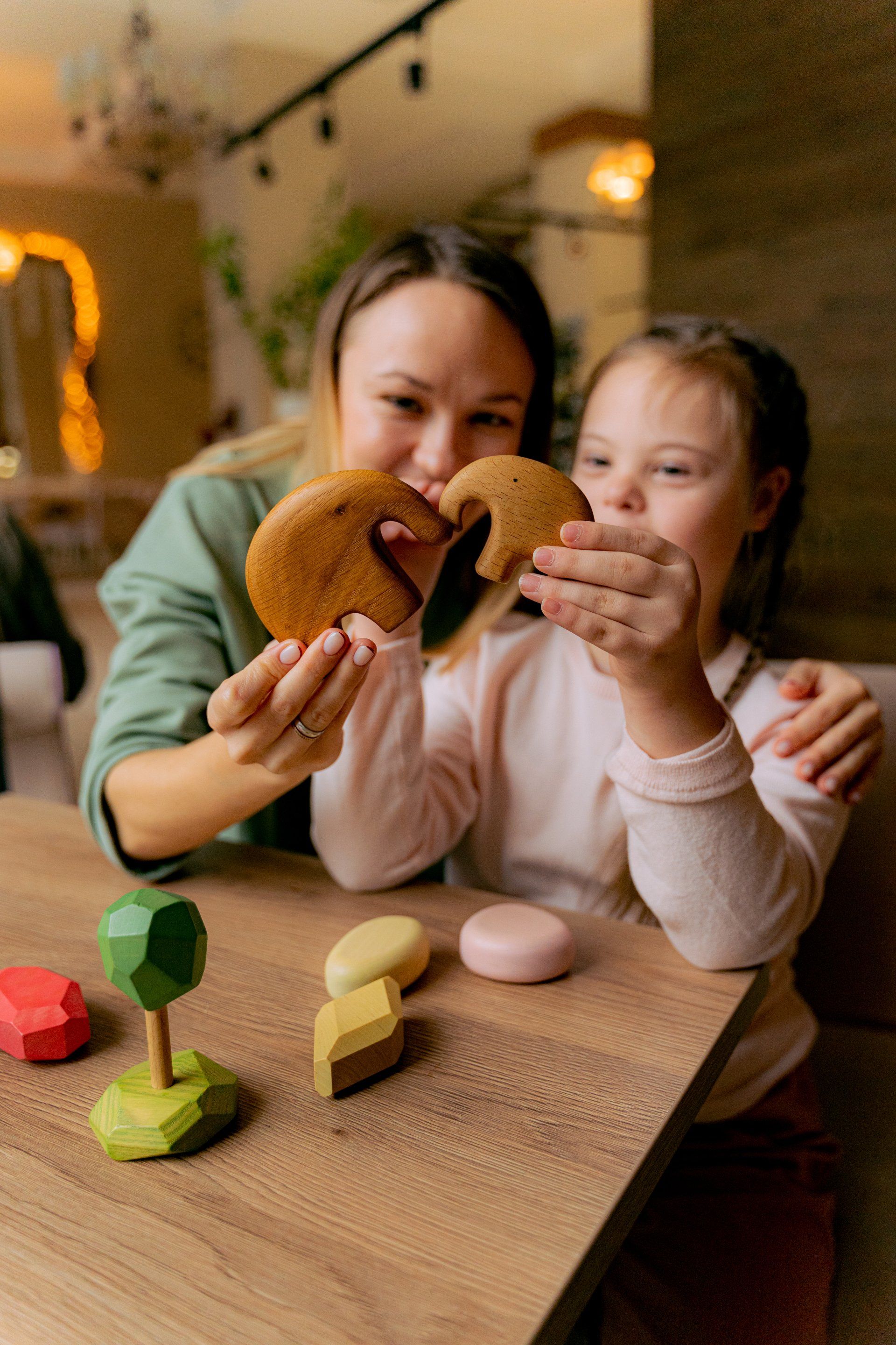 A woman and a little girl are playing with wooden toys at a table.