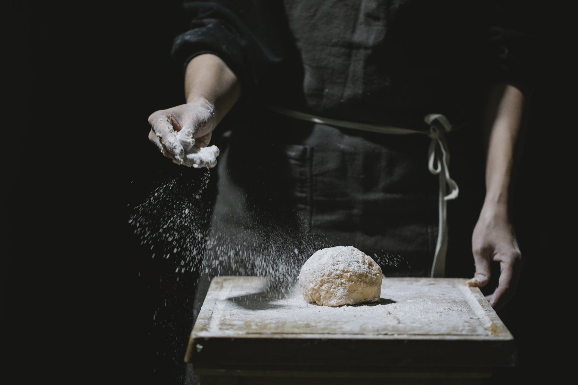 Uma pessoa está polvilhando farinha sobre uma massa sobre uma tábua de cortar.