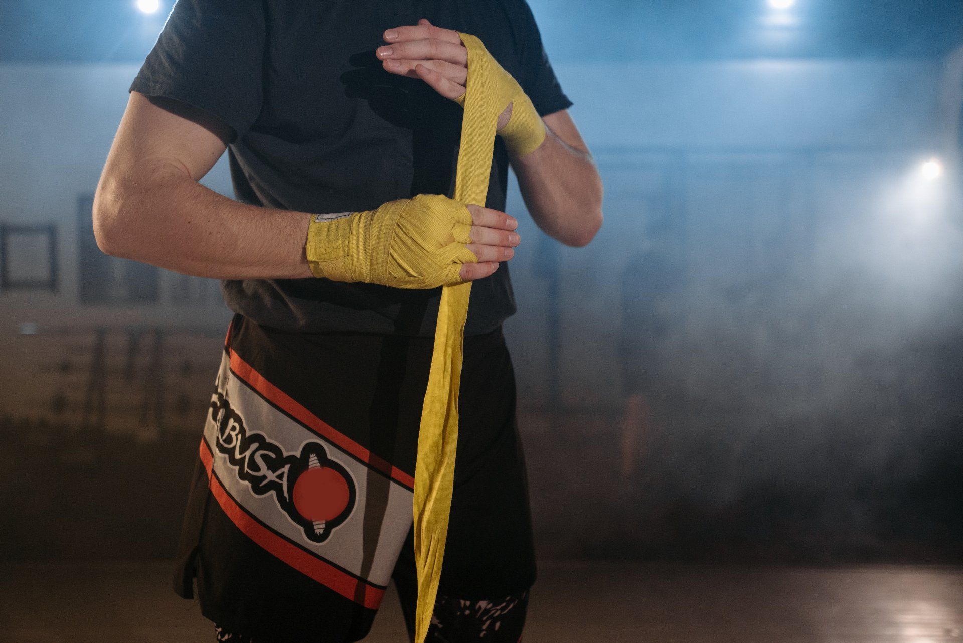 A man is wrapping his hands in yellow boxing wraps.