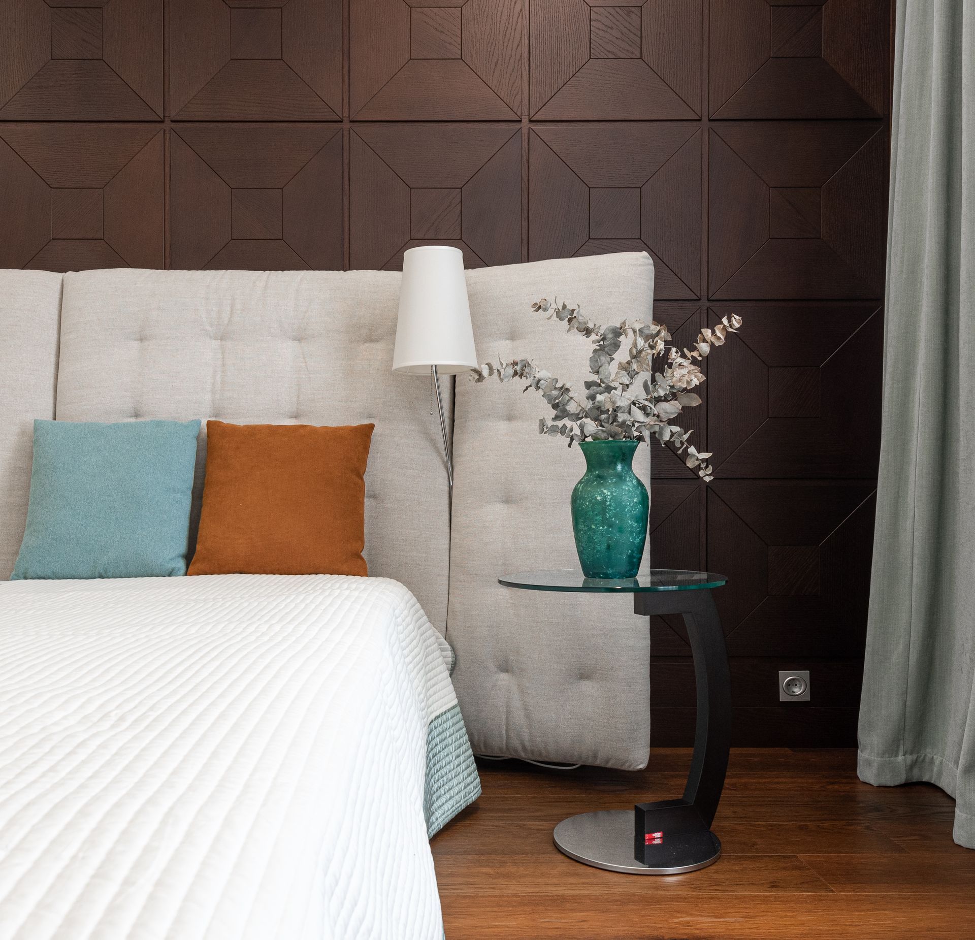simple bed sits in front of a beige cushion headboard that stands in front of a brown tile accent wall.