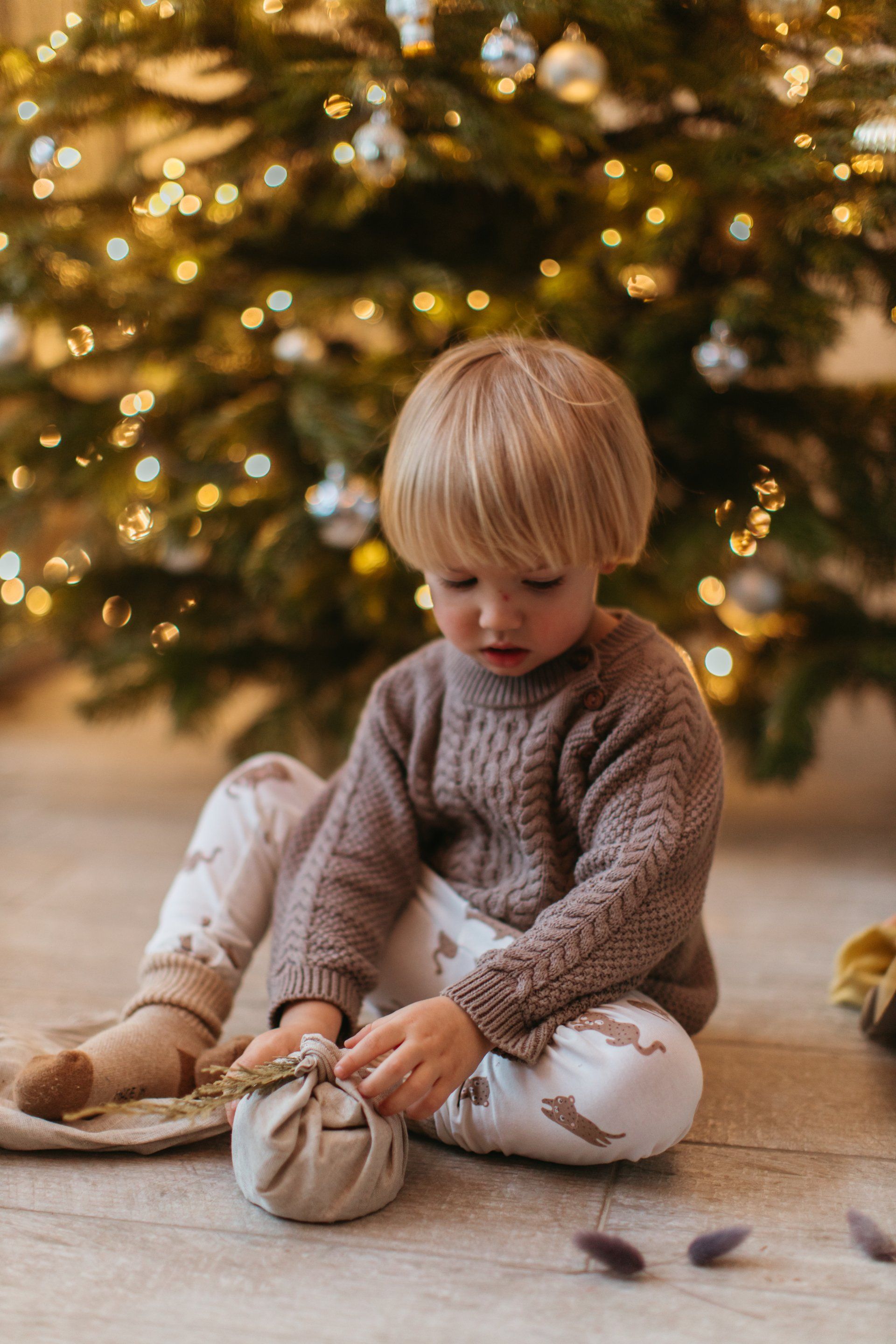 a little boy is sitting on the floor in front of a christmas tree .