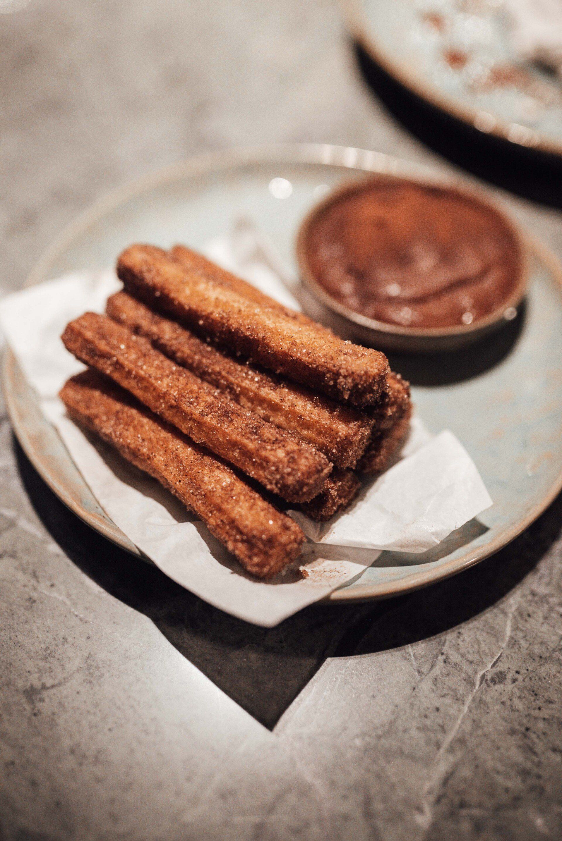 A plate of churros with chocolate sauce on a table.