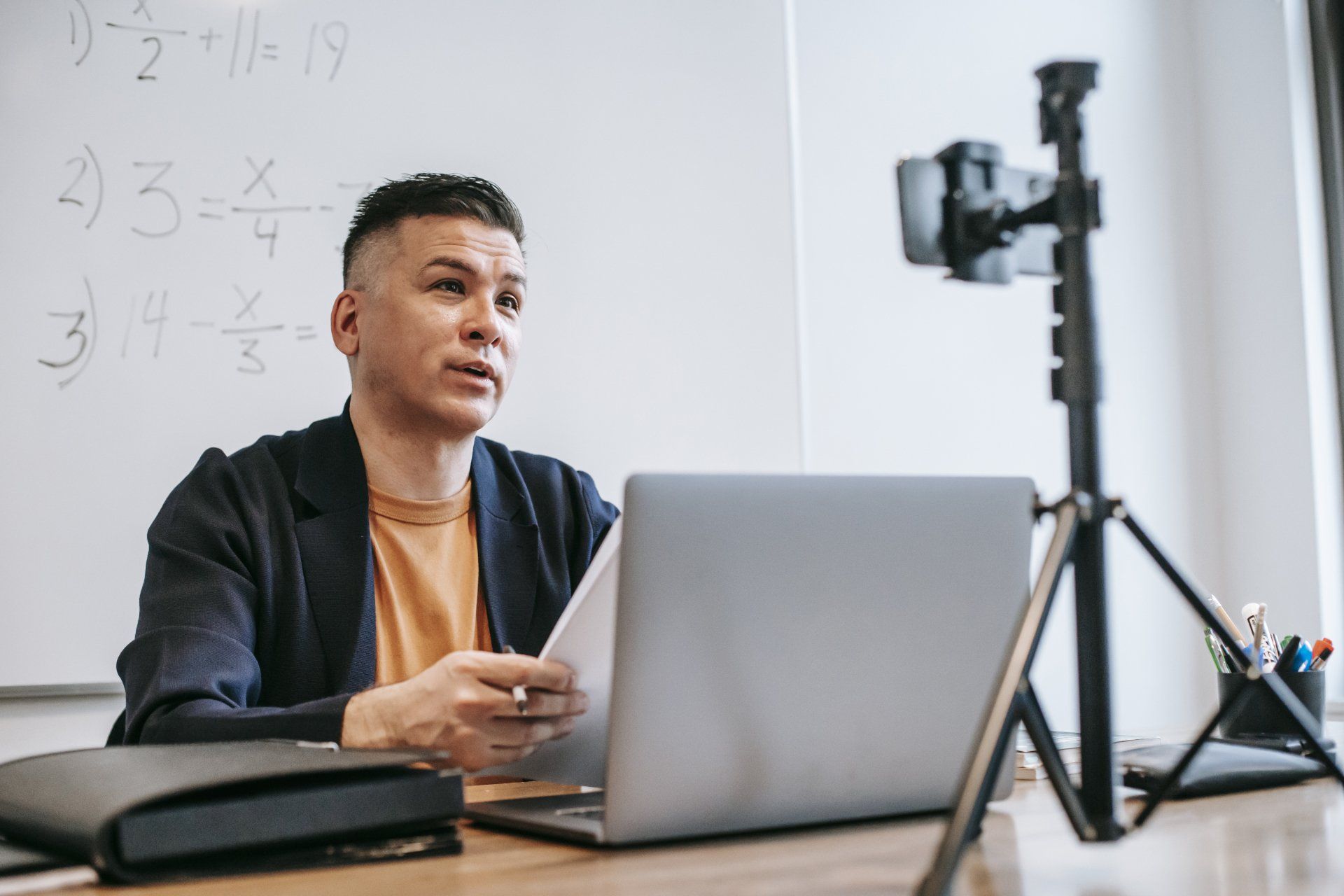 A professor sitting in front of a whiteboard talking to a camera during a virtual event