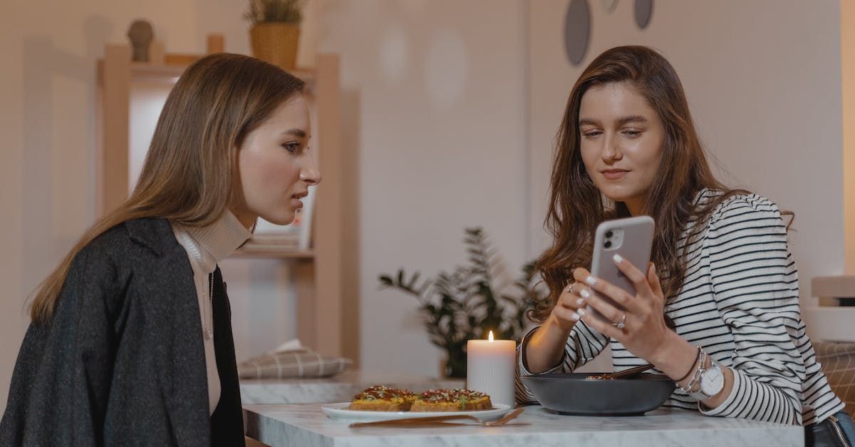 Two women are sitting at a table looking at a cell phone.