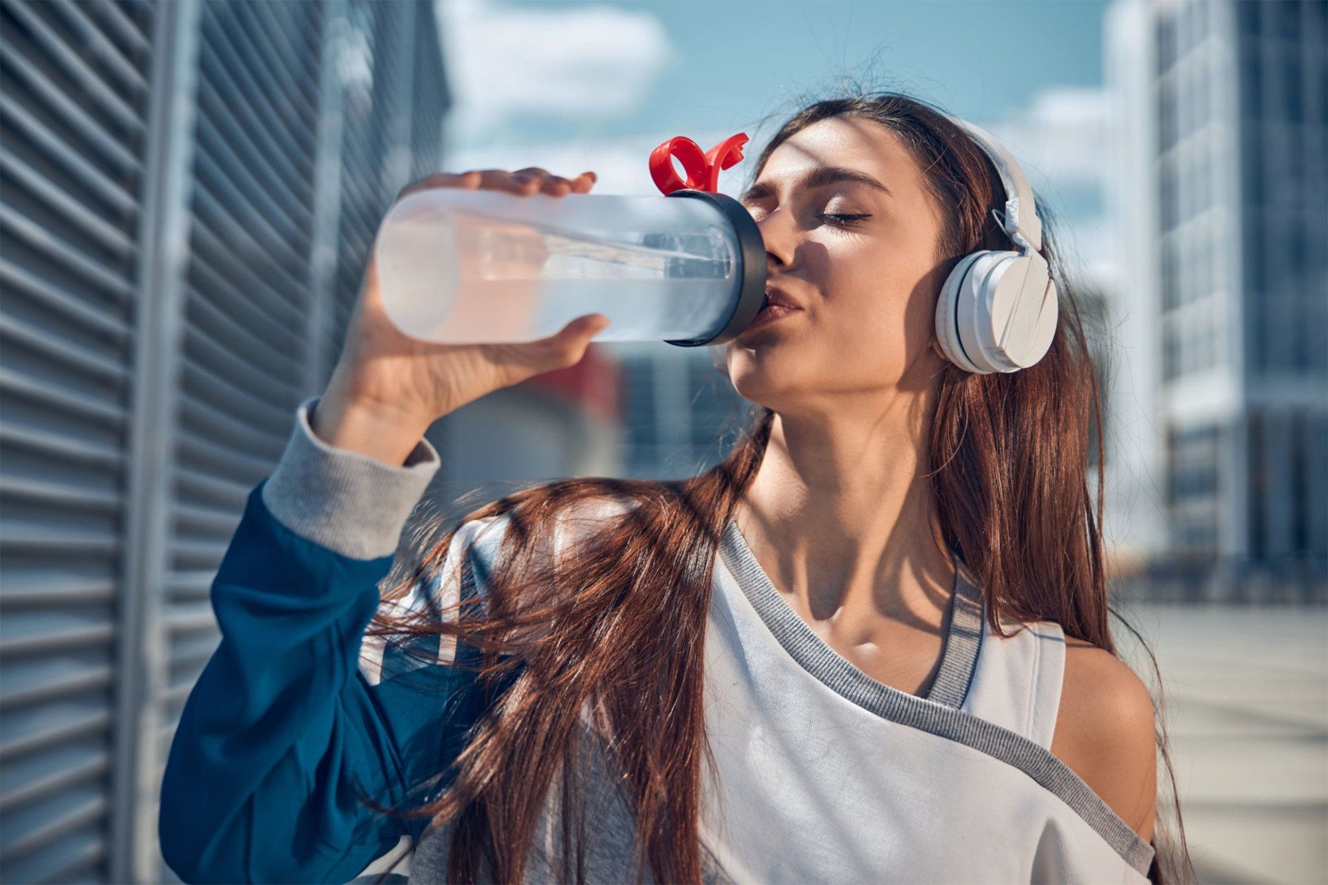 A woman wearing headphones is drinking water from a bottle.