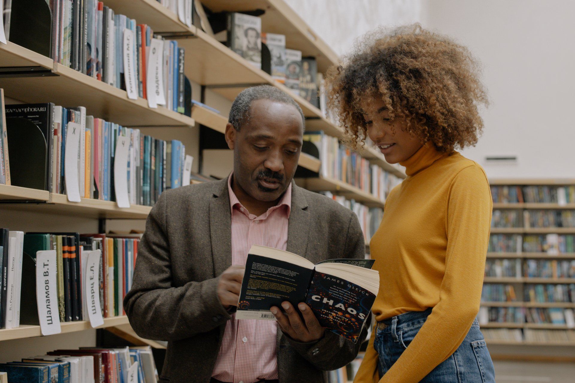 A man and a woman are looking at a book in a library.