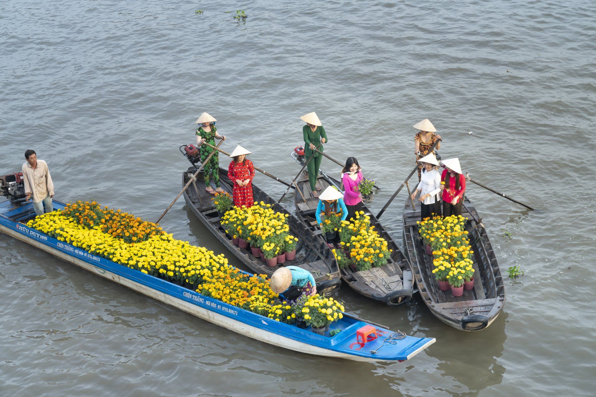 A group of people are rowing boats filled with flowers.