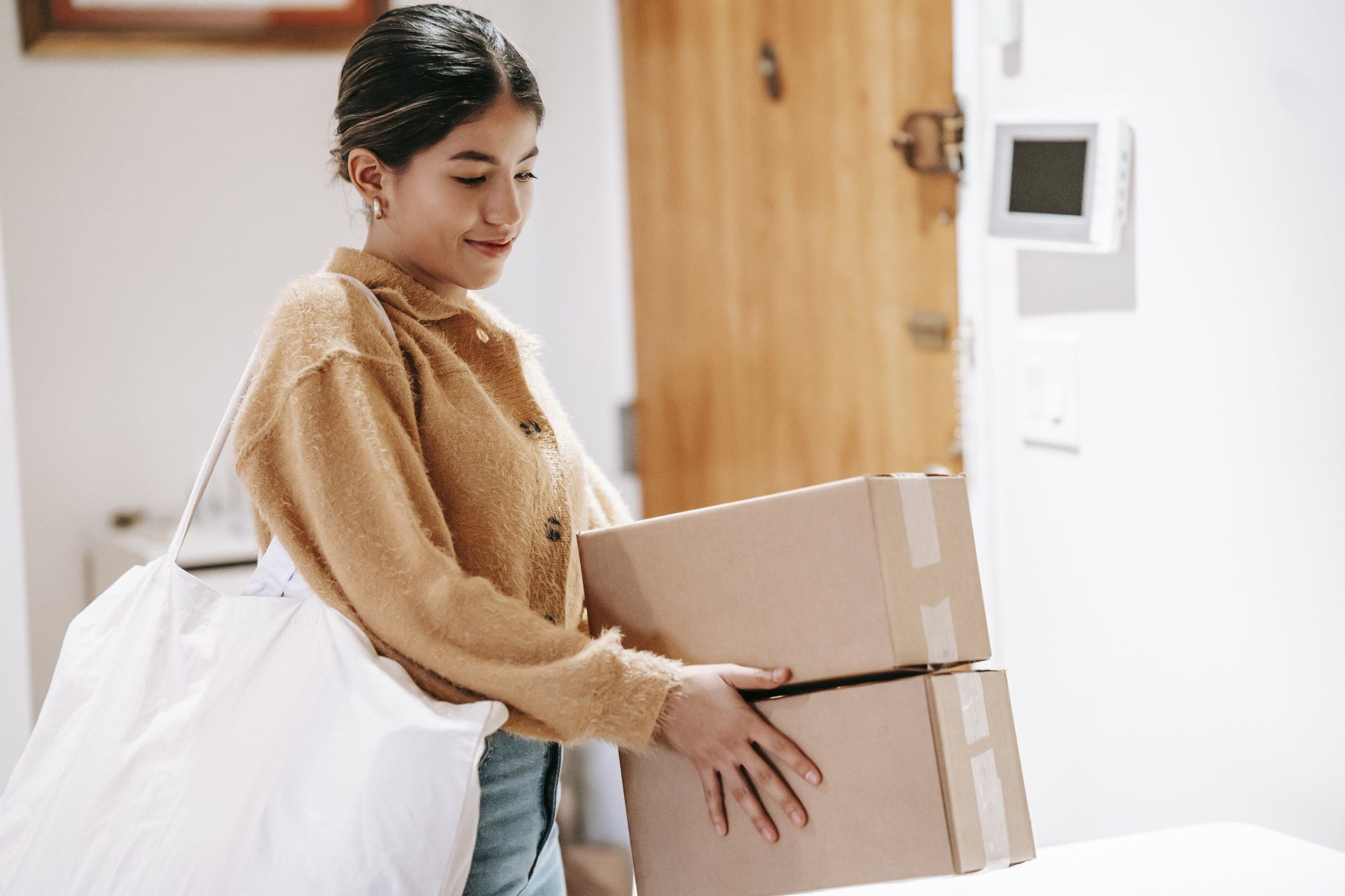 Vrouw met beige jas en grote witte shopper houdt twee postpakketten vast