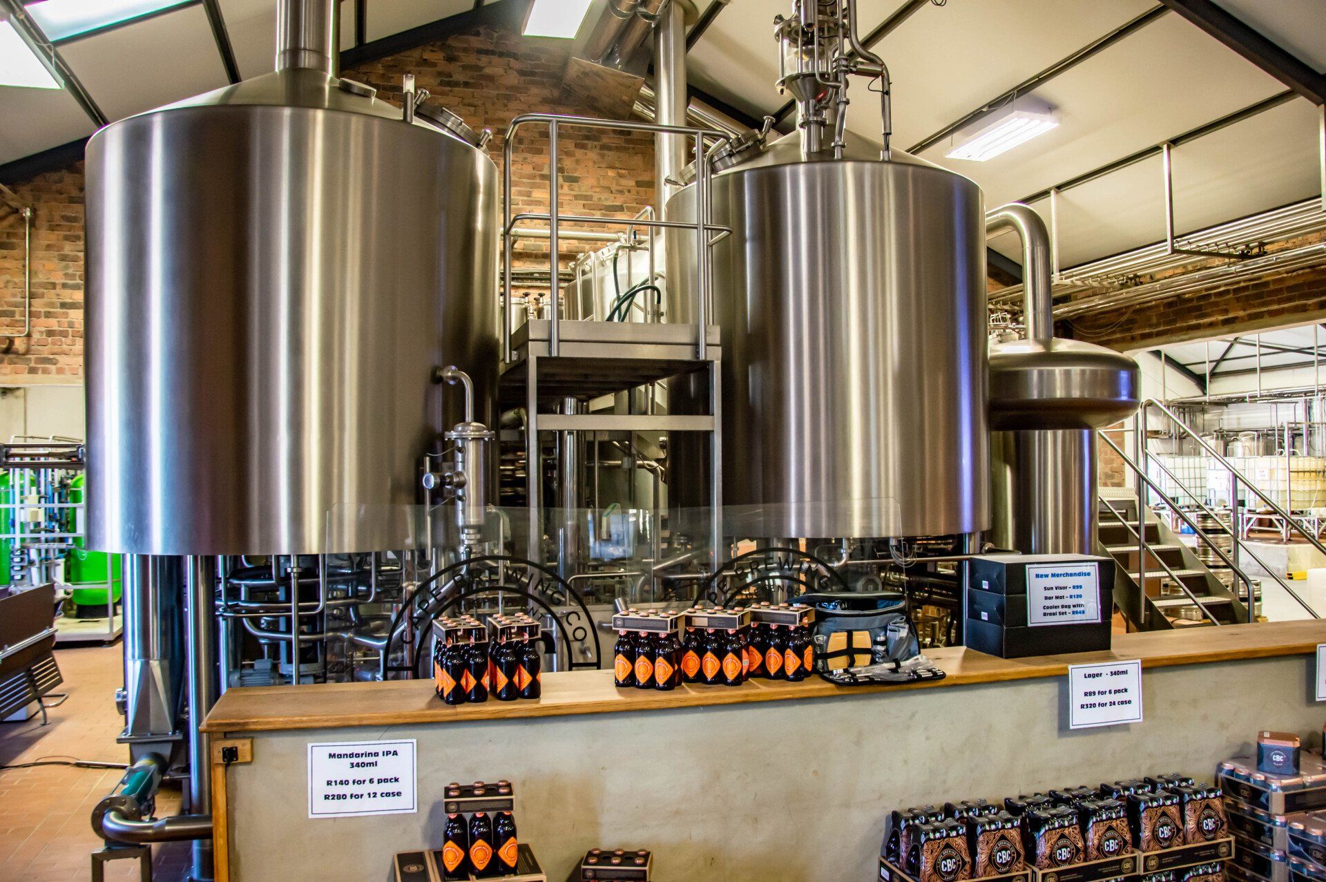 A brewery with a lot of stainless steel tanks and bottles on the counter.
