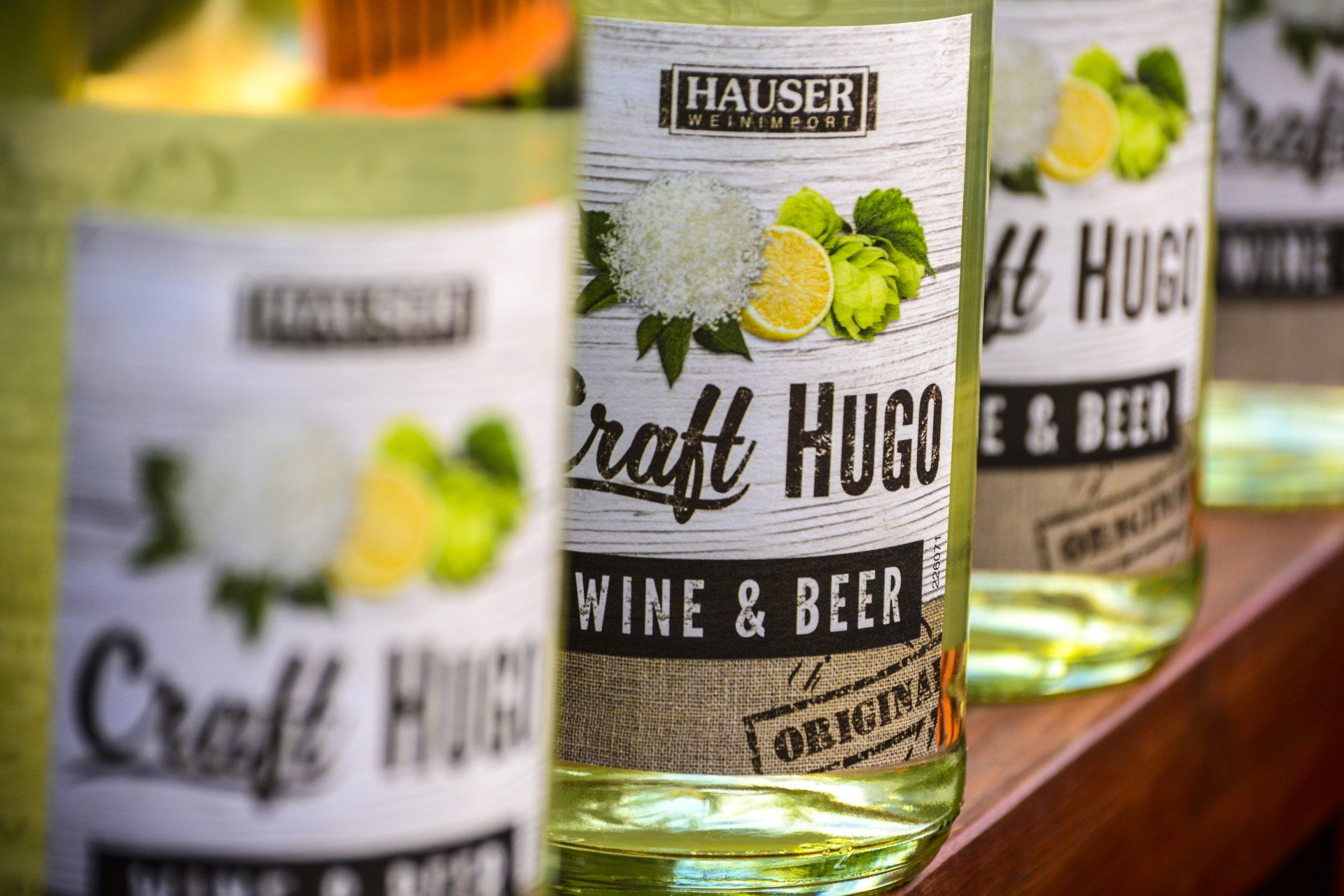 Three bottles of craft hugo wine and beer are lined up on a wooden shelf.