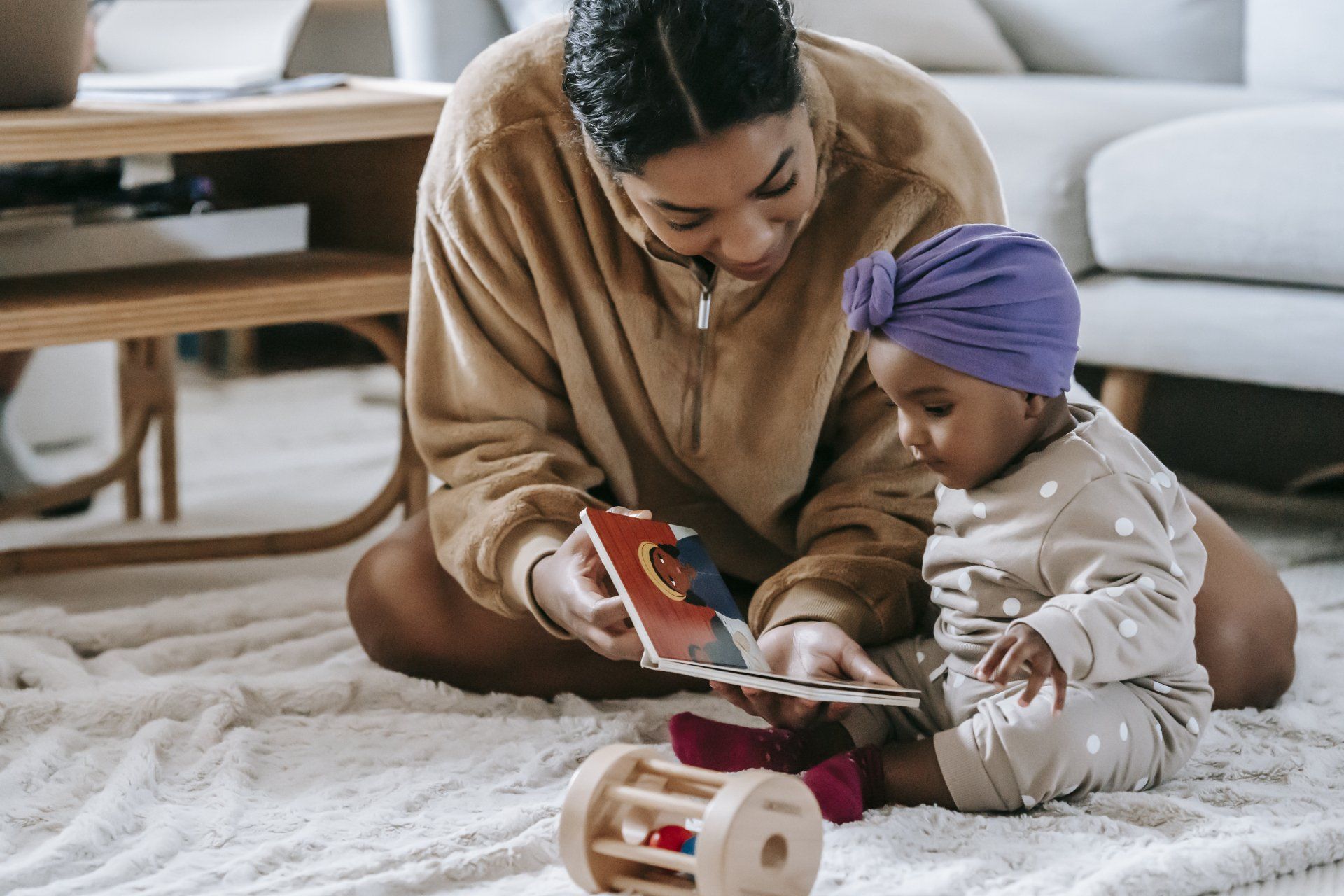 A woman is sitting on the floor reading a book to a baby.
