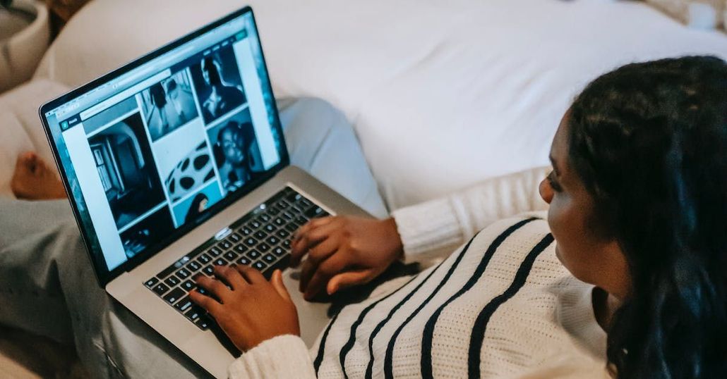 A woman is sitting on a bed using a laptop computer.