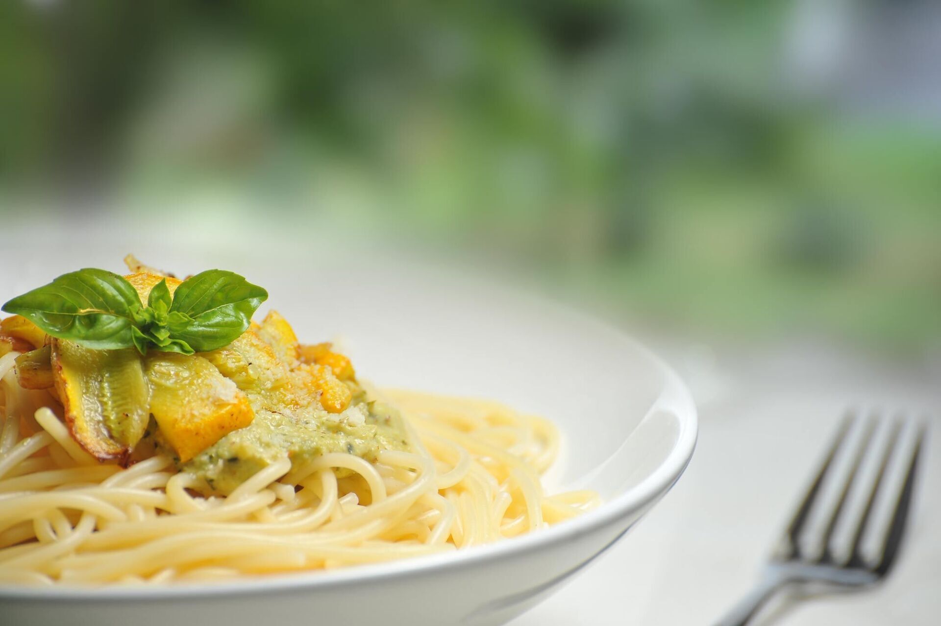 A bowl of spaghetti with vegetables and a fork on a table.