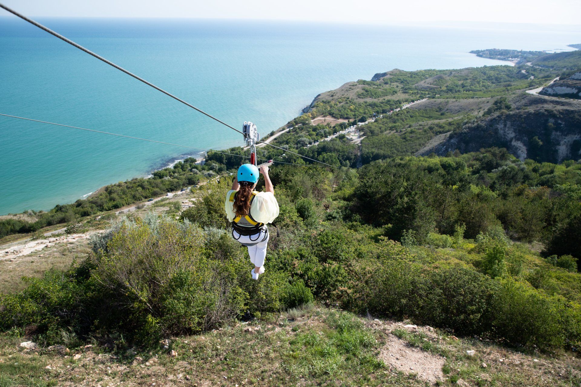 A woman is riding a zip line over a hill.