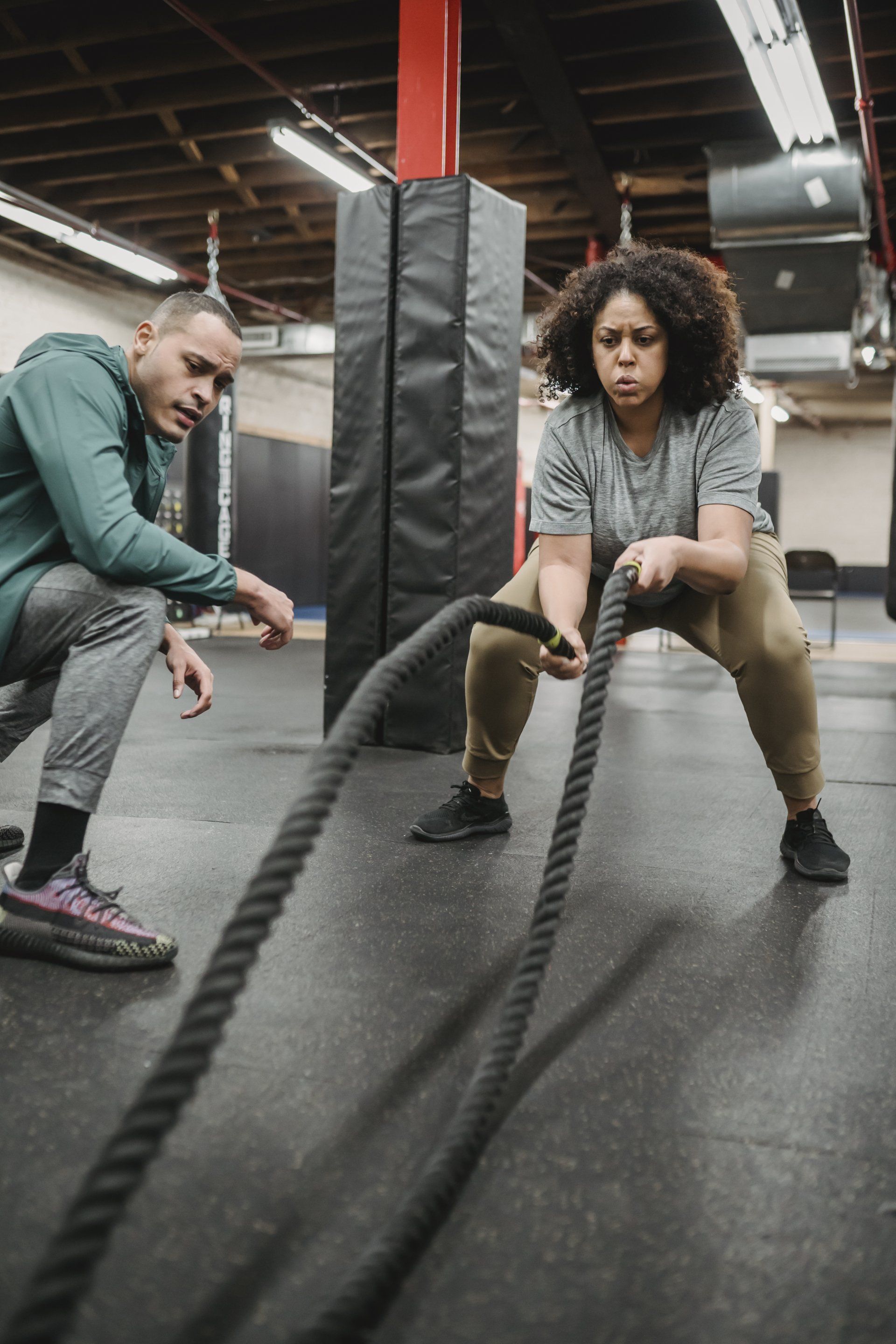 A man and a woman are playing with ropes in a gym.