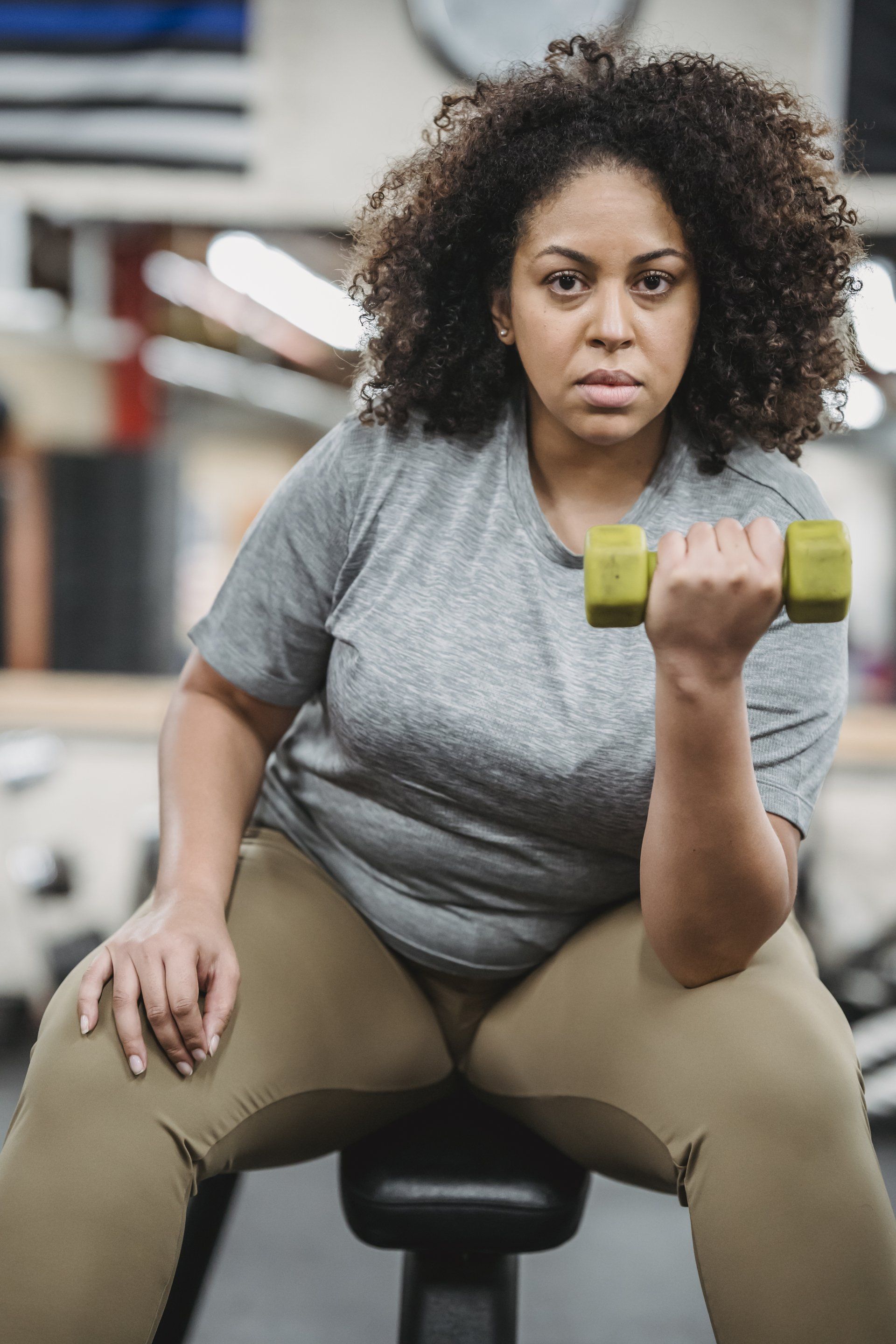 A woman is sitting on a bike in a gym holding a dumbbell.