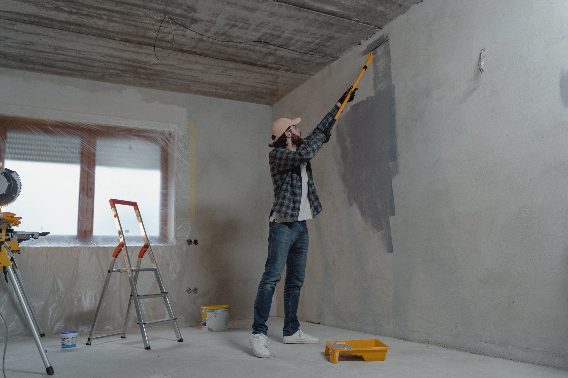 A man painting a concrete wall with a roller brush.