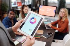 A person is holding a tablet with a pie chart on it.