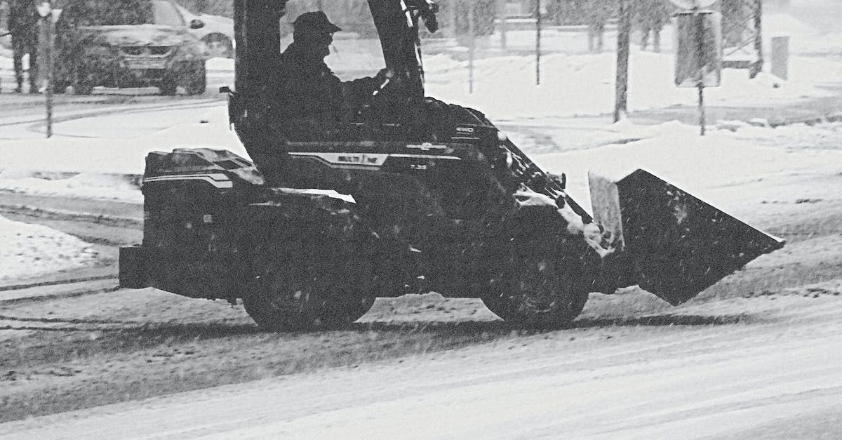 a black and white photo of a man driving a snow plow on a snowy street .