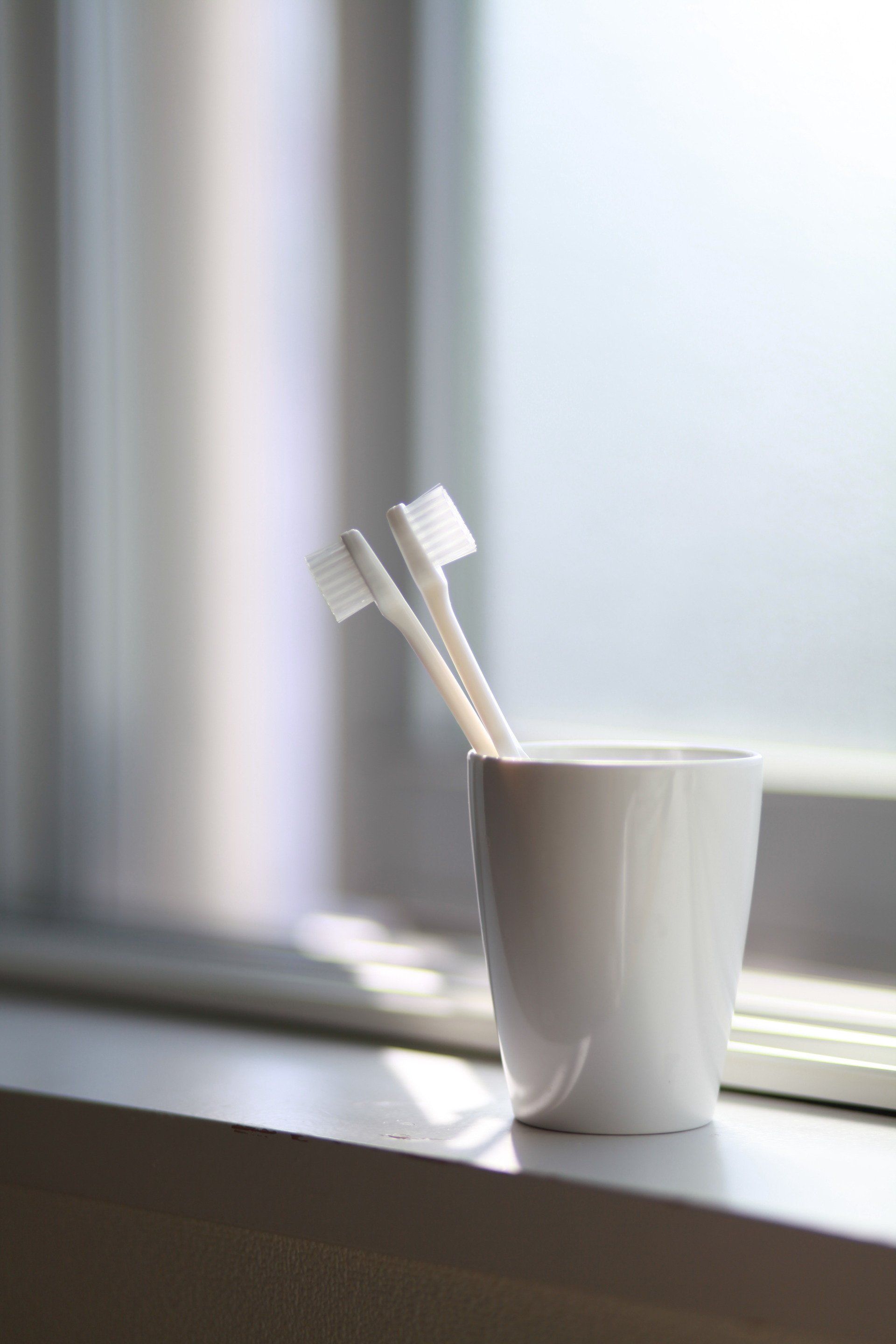 two toothbrushes are in a cup on a window sill .