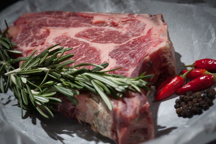 A piece of raw grass fed lamb with rosemary and red peppers on a plate.