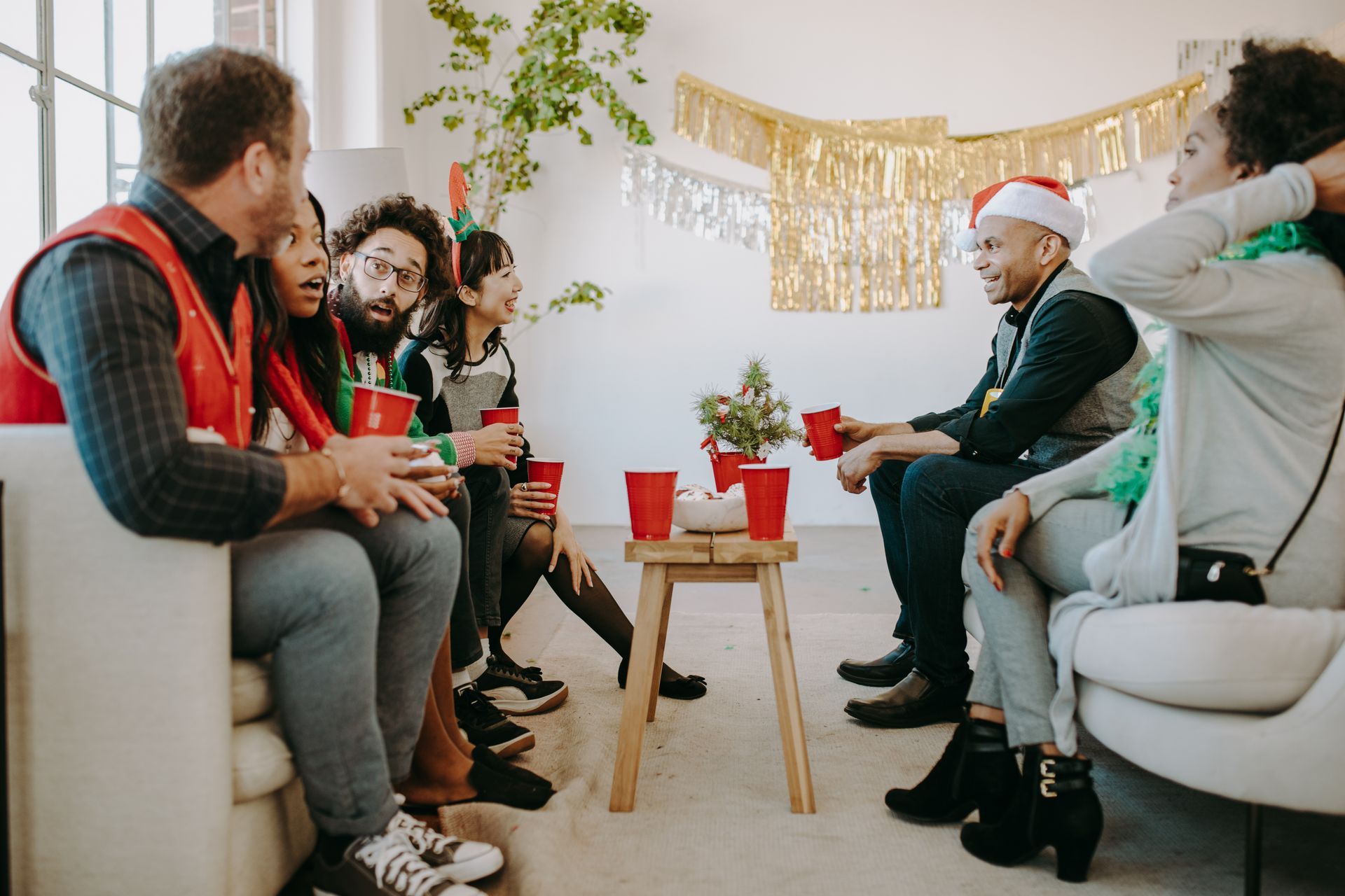 Group of diverse people at a holiday party, drinking from red cups, festive decorations, smiling.