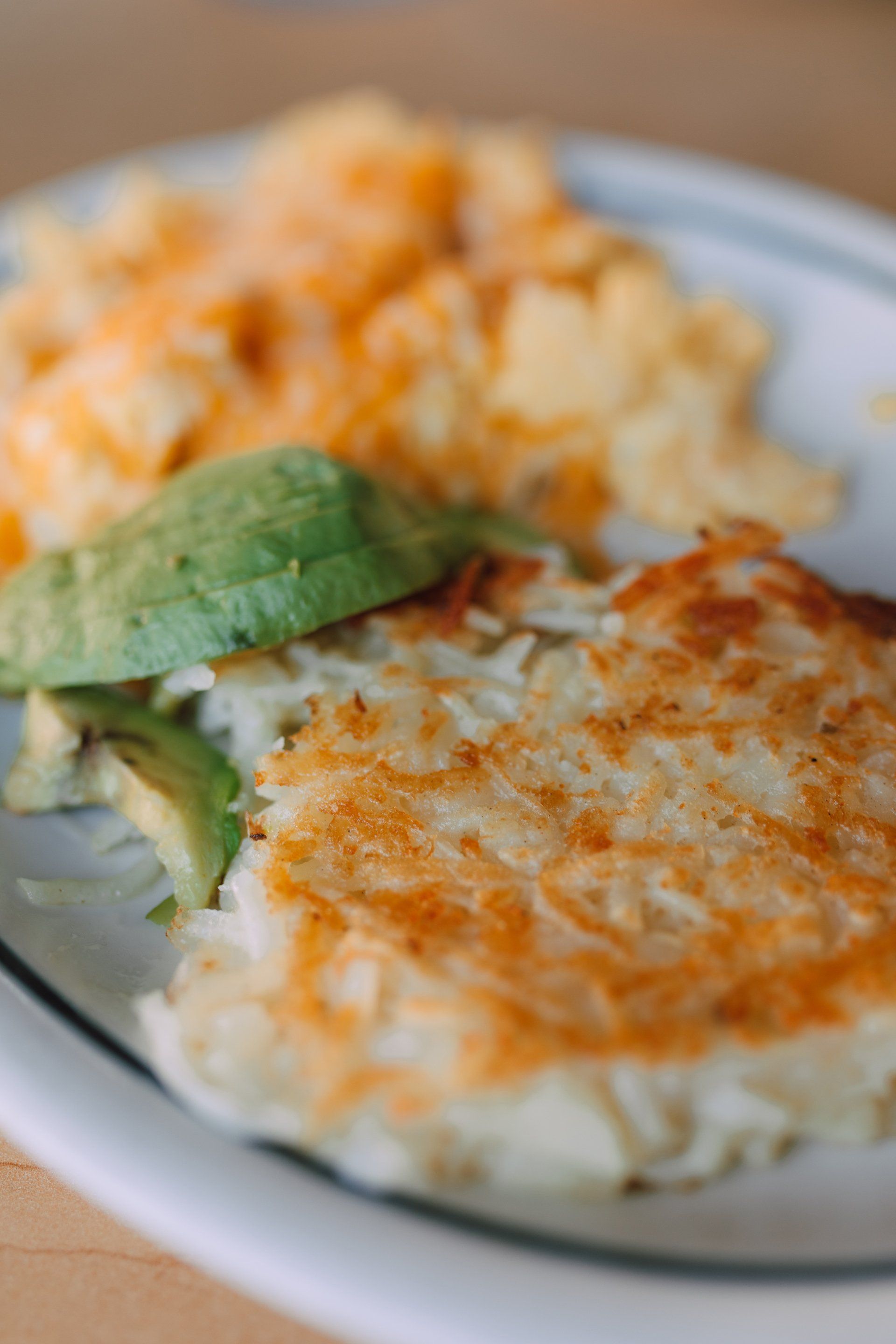 A close up of a plate of food with hash browns , macaroni and cheese and avocado.