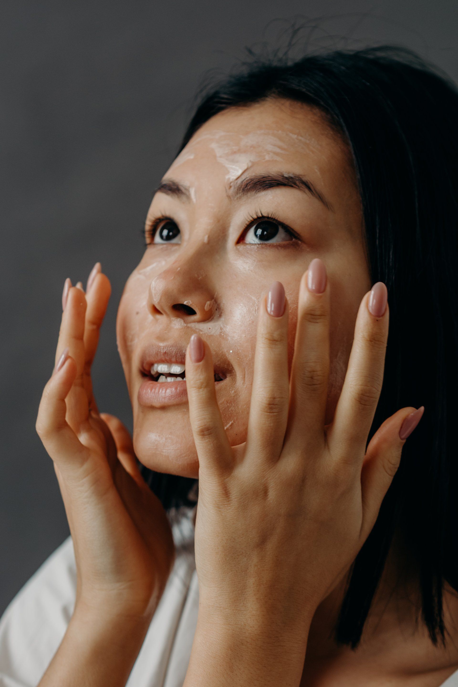 A woman is applying lotion to her face with her hands.