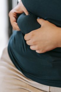 A person is holding their belly with their hands.