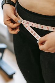 A woman is measuring her waist with a tape measure.