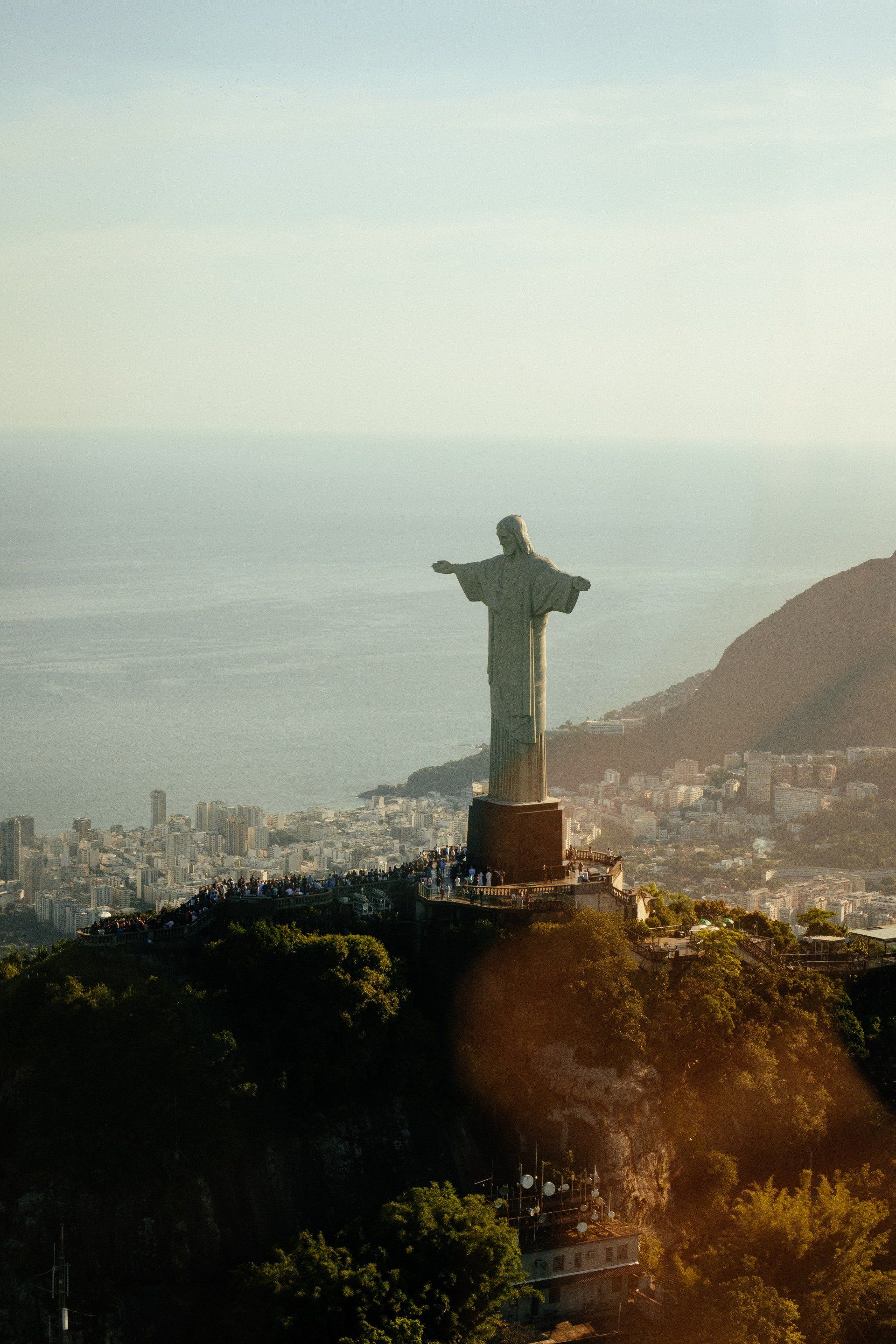 A statue of jesus is standing on top of a hill overlooking the ocean.