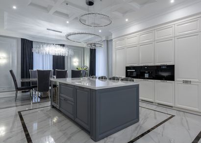 Modern white kitchen with a large island. The island has a wood panel front, white countertop, and herbs on top.