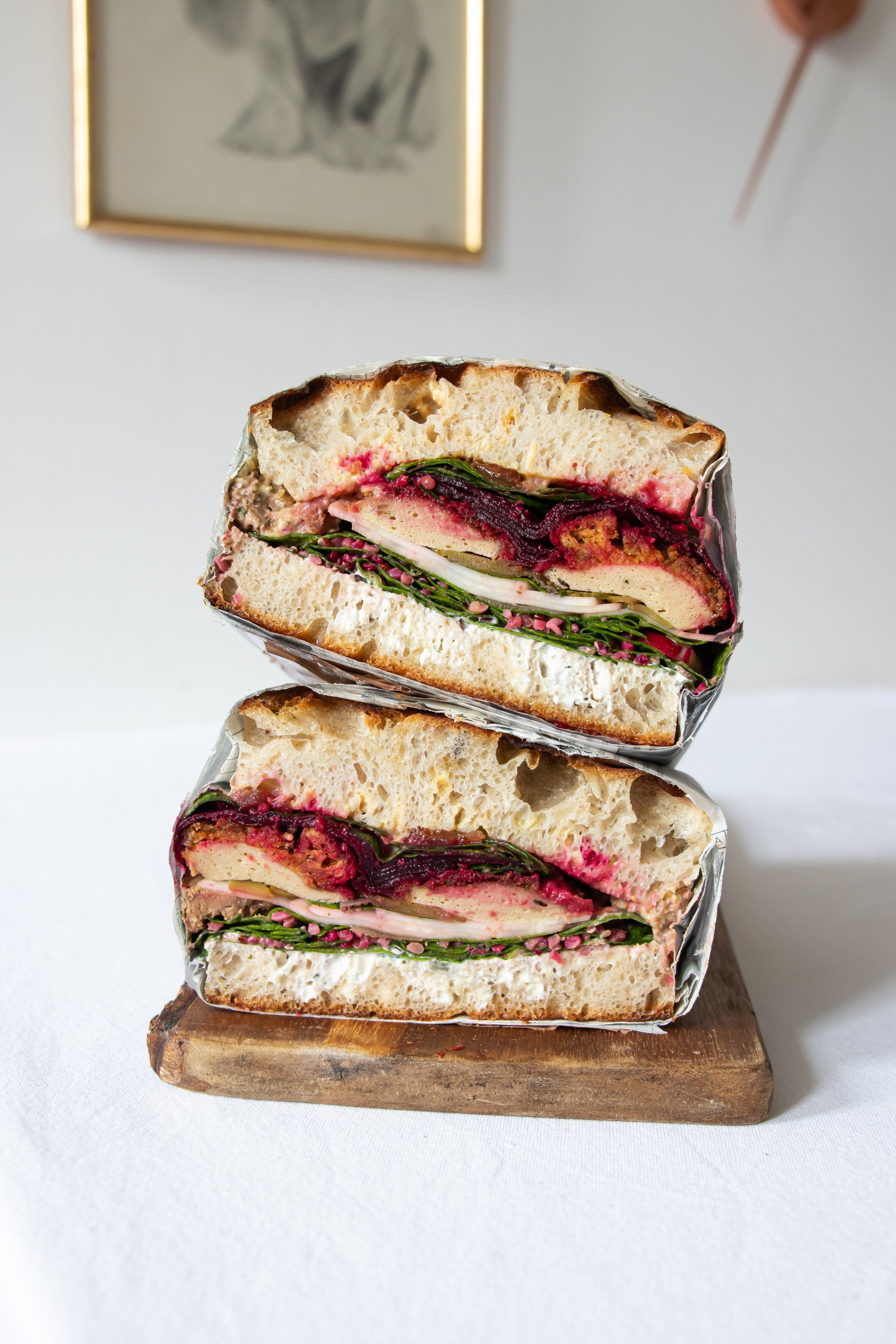 Two sandwiches are stacked on top of each other on a wooden cutting board.