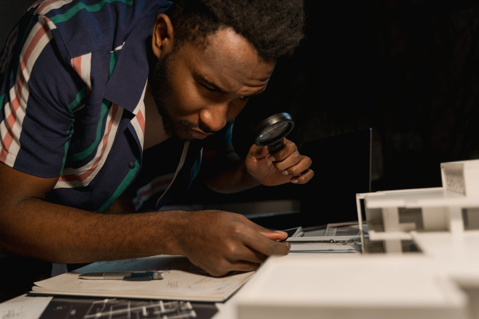 A man is looking through a magnifying glass at a model of a house.