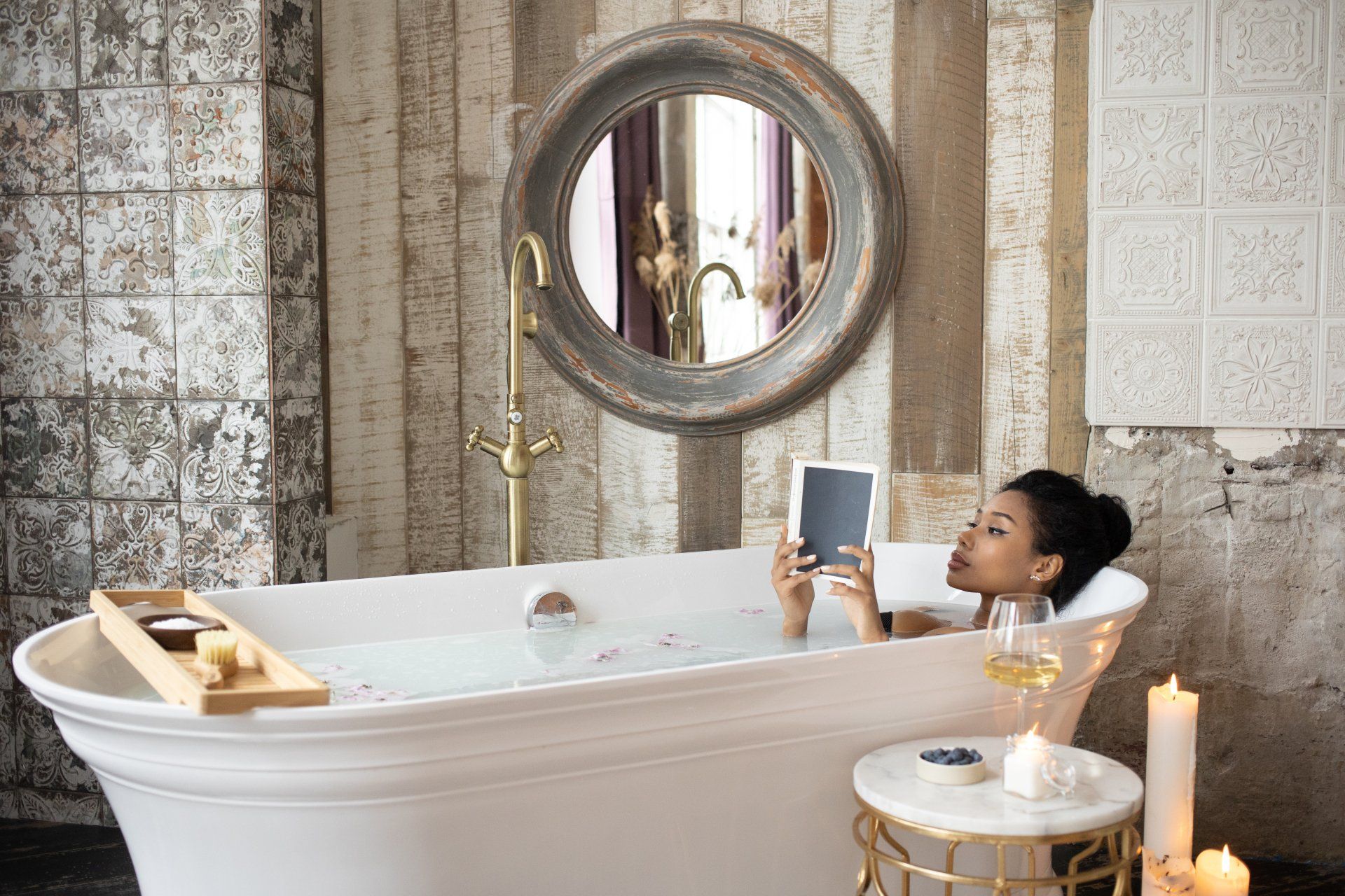 a woman is taking a bath in a bathtub while looking at a tablet . Bathroom Remodeling Trends for 2024