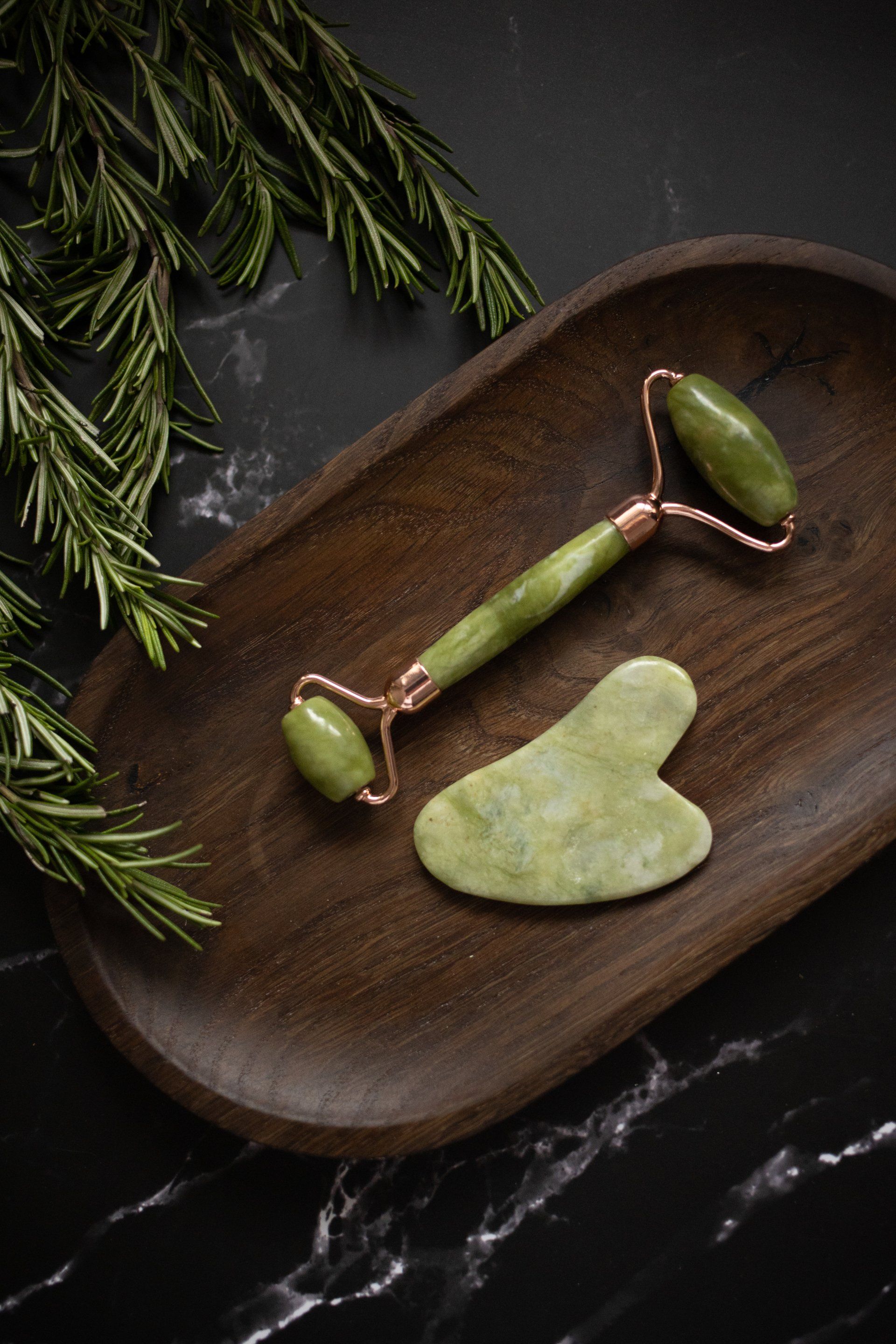 a jade roller and gua sha on a wooden tray .