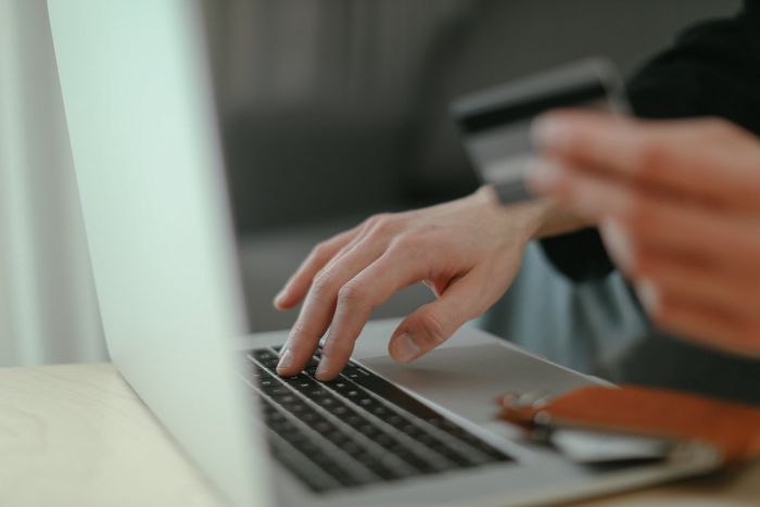 A person is holding a credit card while typing on a laptop.