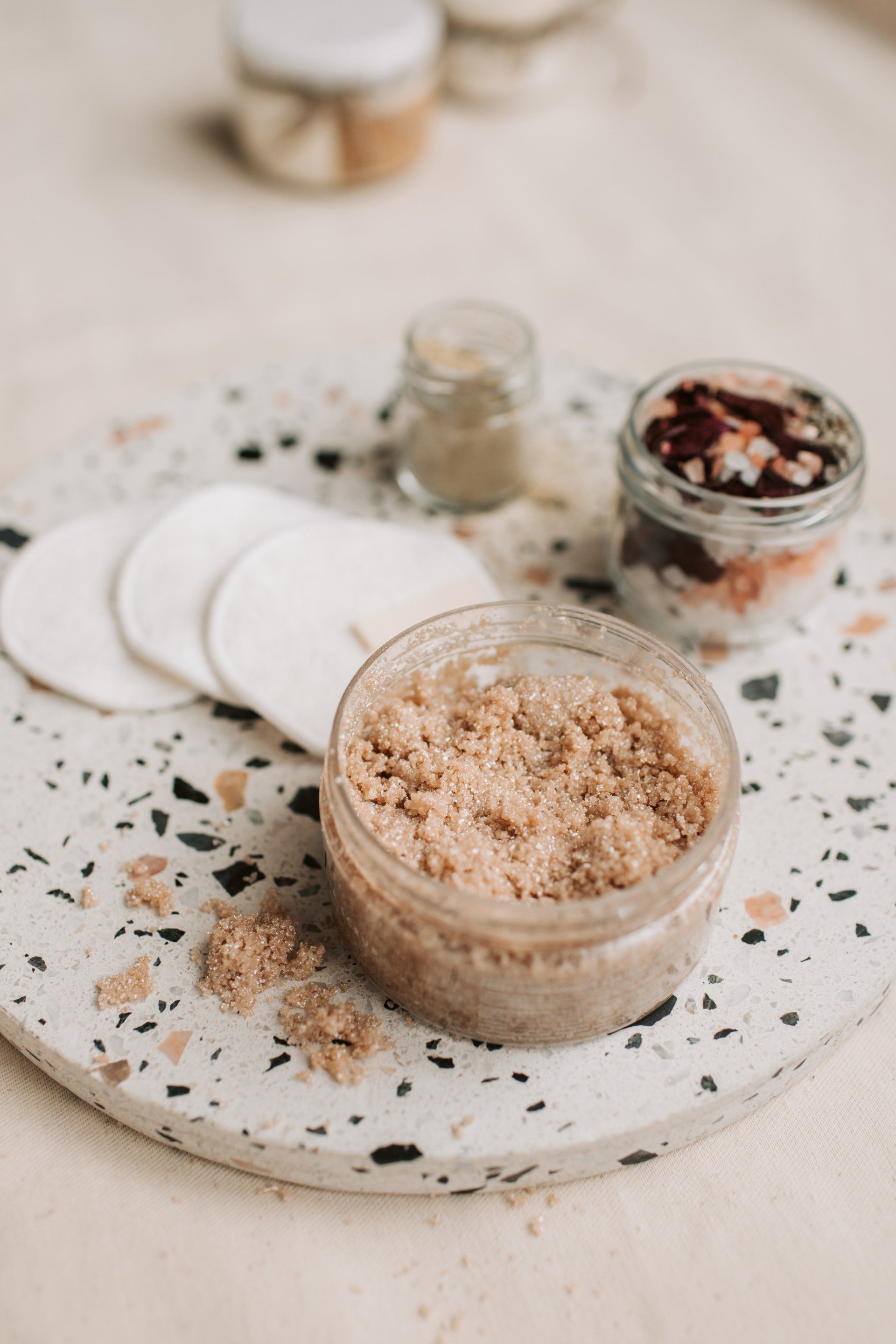 A jar of body scrub is sitting on a marble tray on a table.