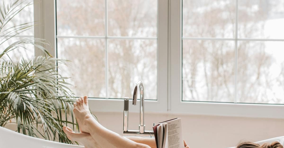 A woman is laying in a bathtub reading a book.