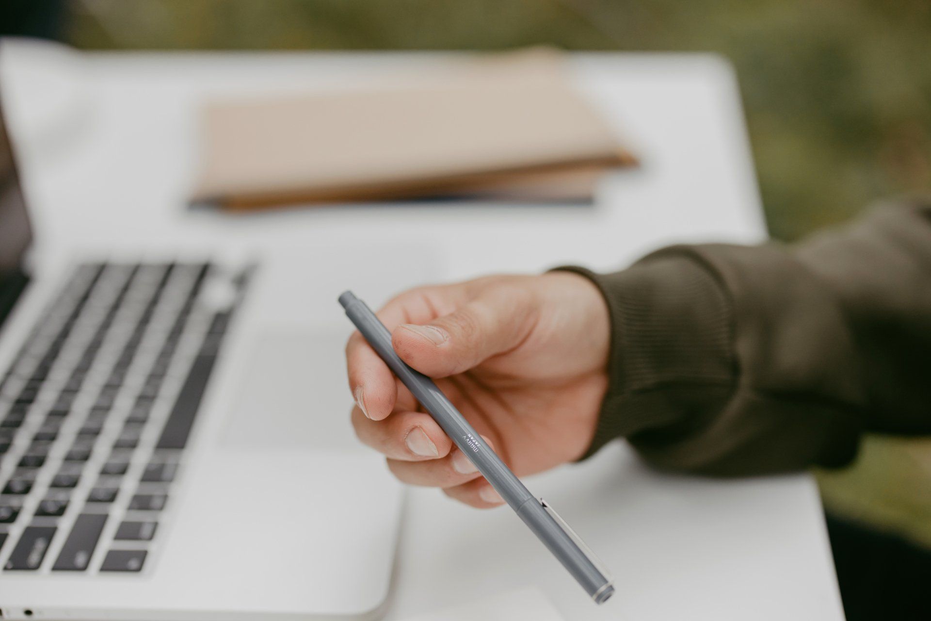 A person is holding a pen in front of a laptop computer.