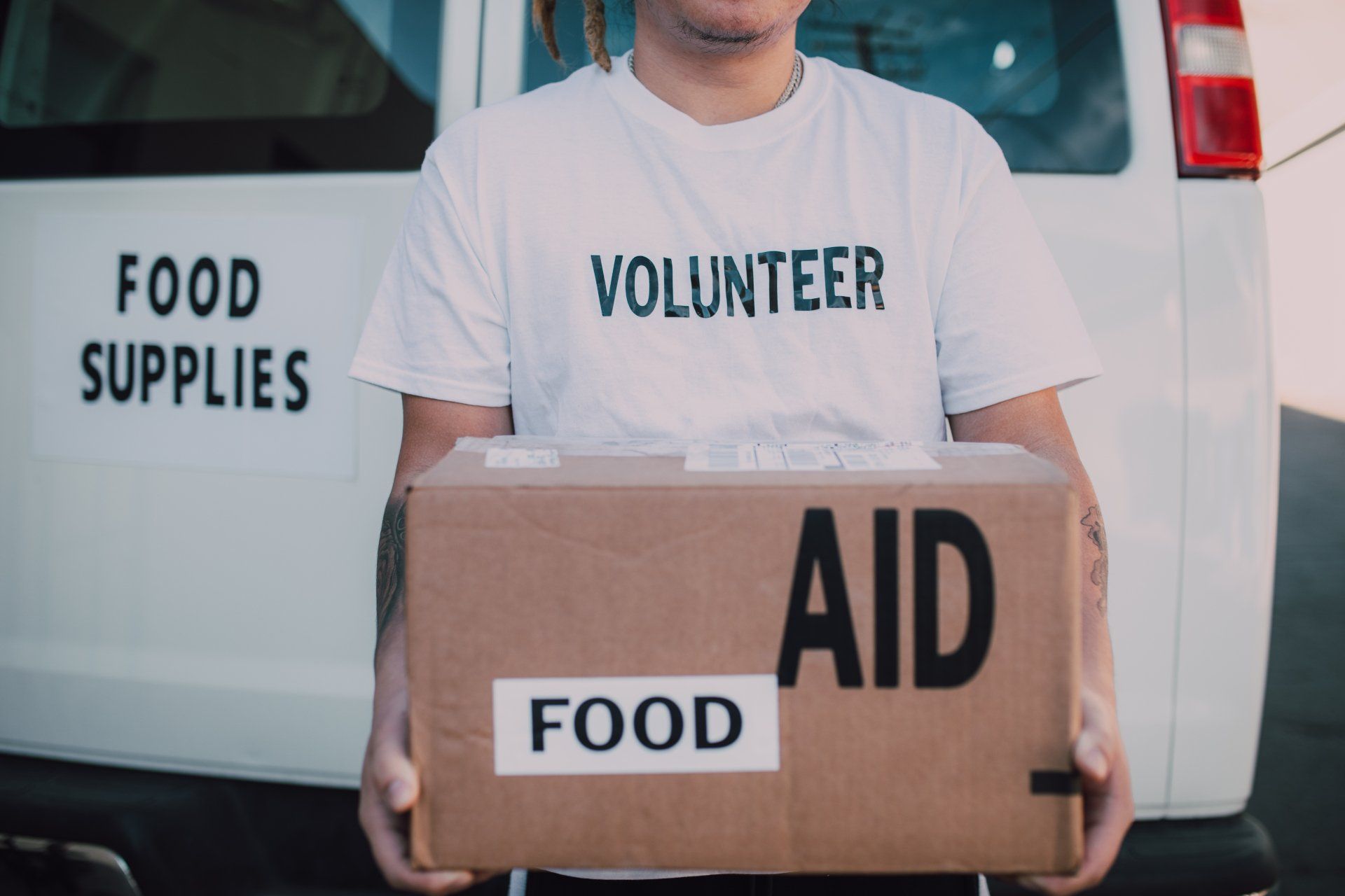 a volunteer is holding a box of food in front of a food supplies van .