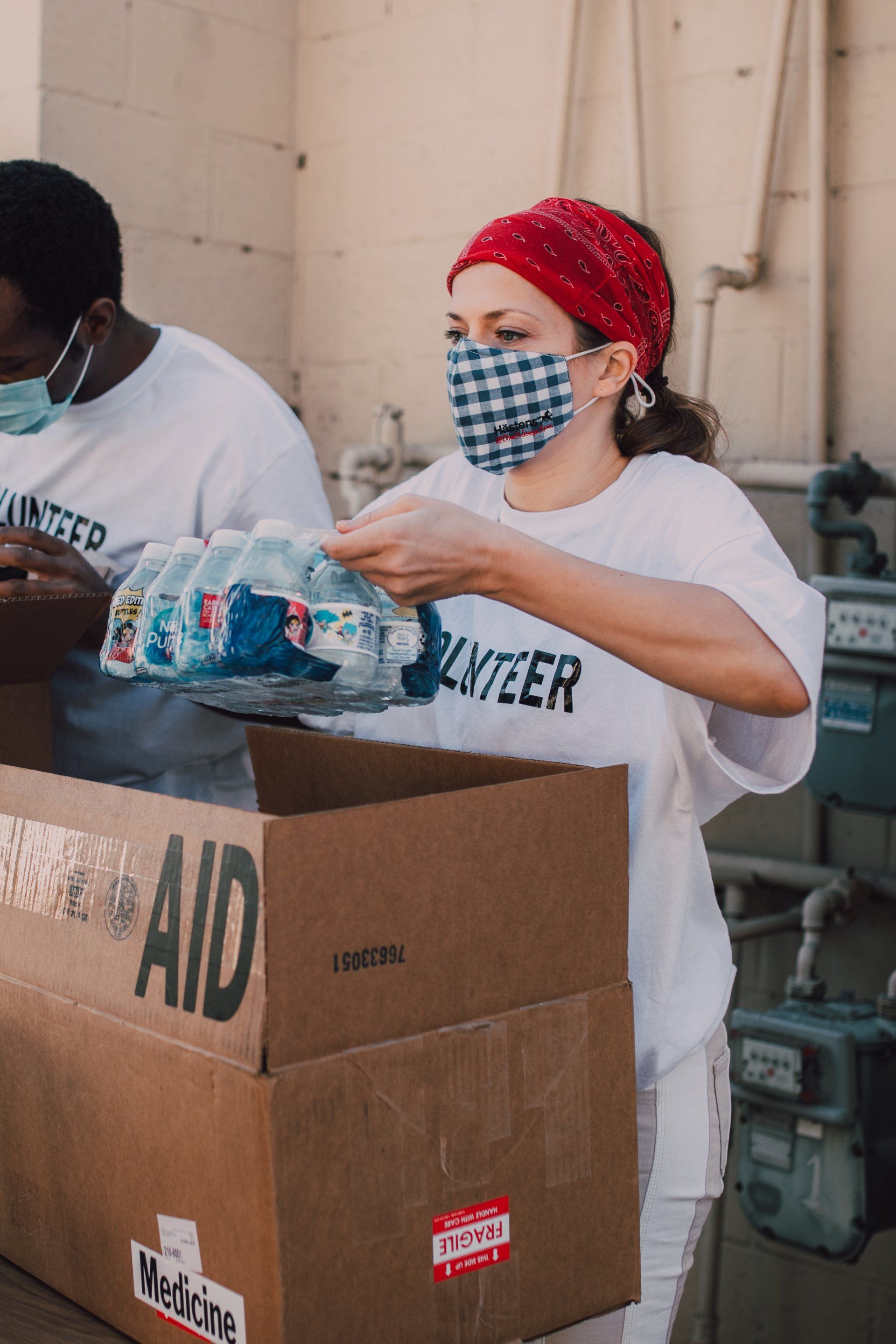 A woman wearing a mask is giving away bottles of water in a cardboard box at a Bethel Baptist Church missions event.