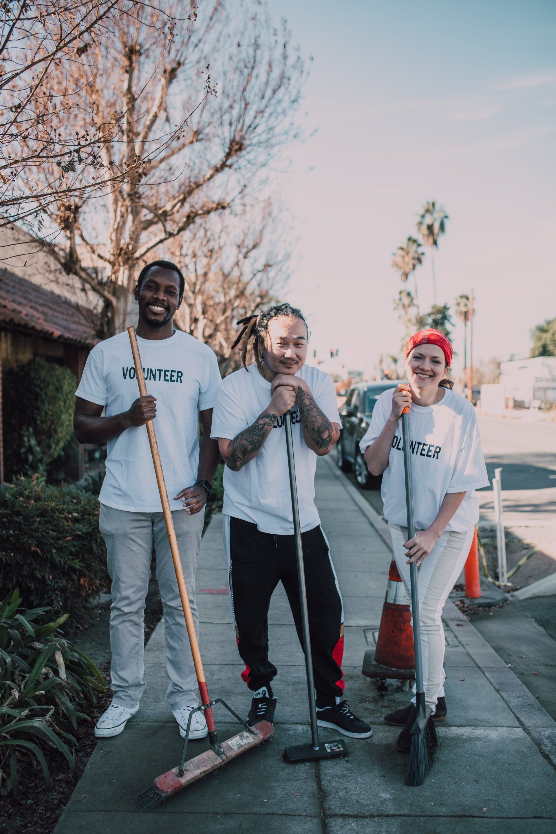 A group of people are standing on a sidewalk holding brooms.