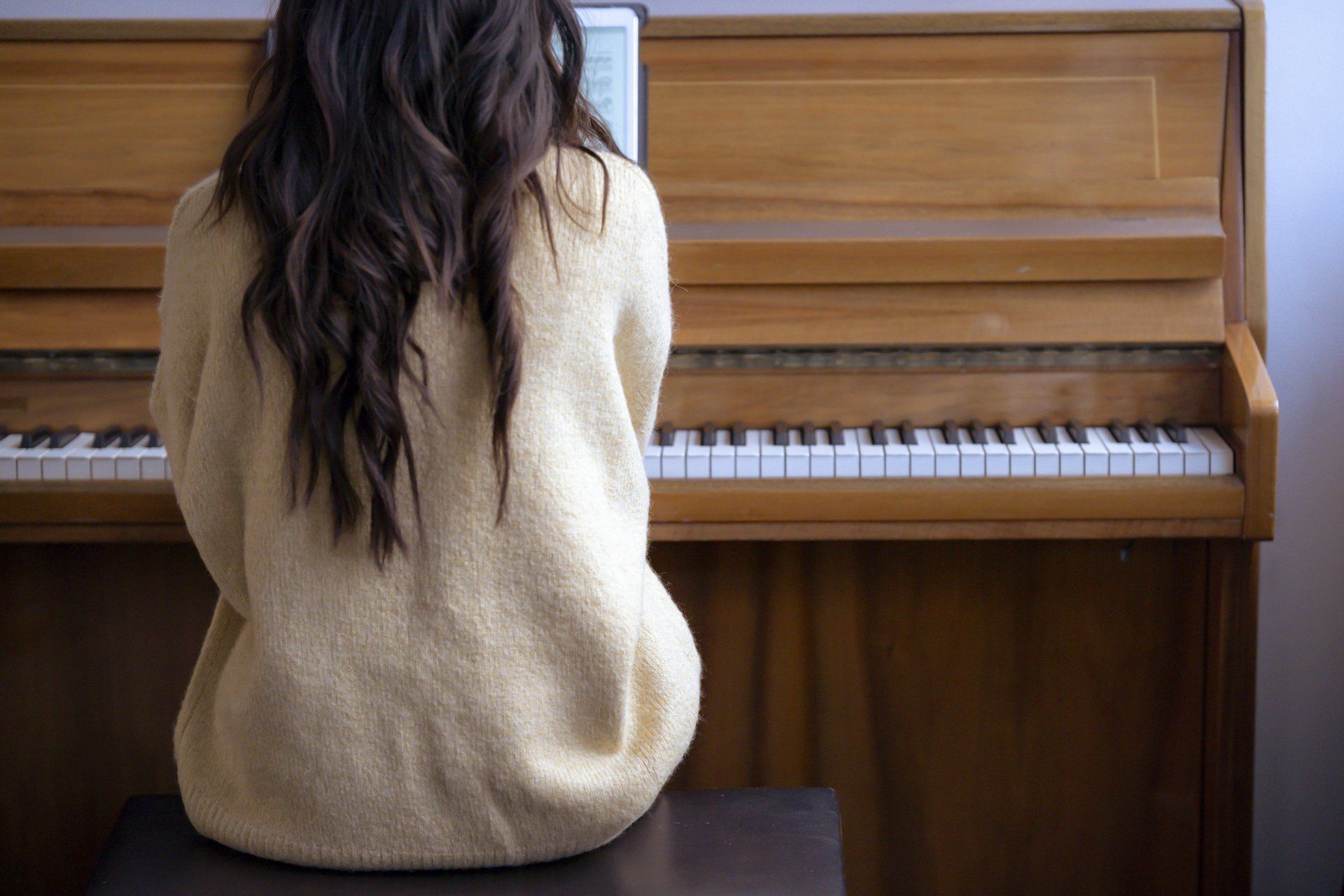 Une femme est assise devant un piano, dos à la caméra.