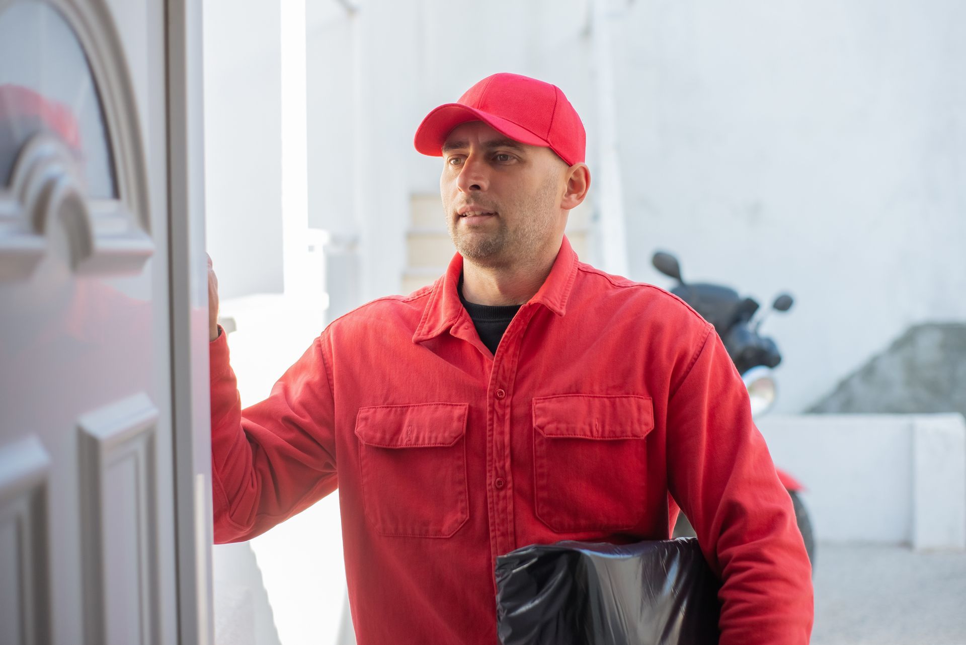 A delivery man is holding a black bag and standing in front of a door.