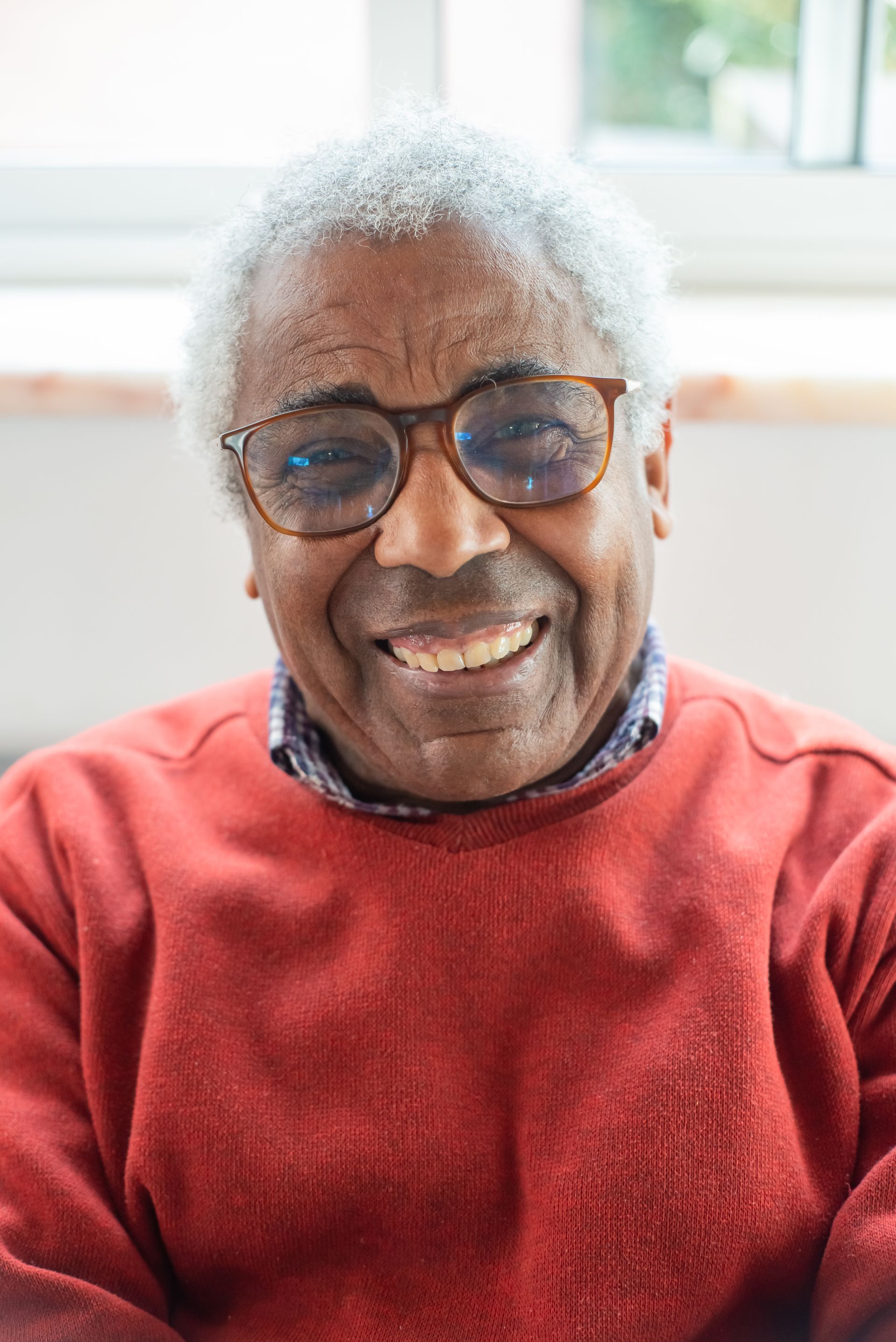 An older man wearing glasses and a red sweater is smiling.