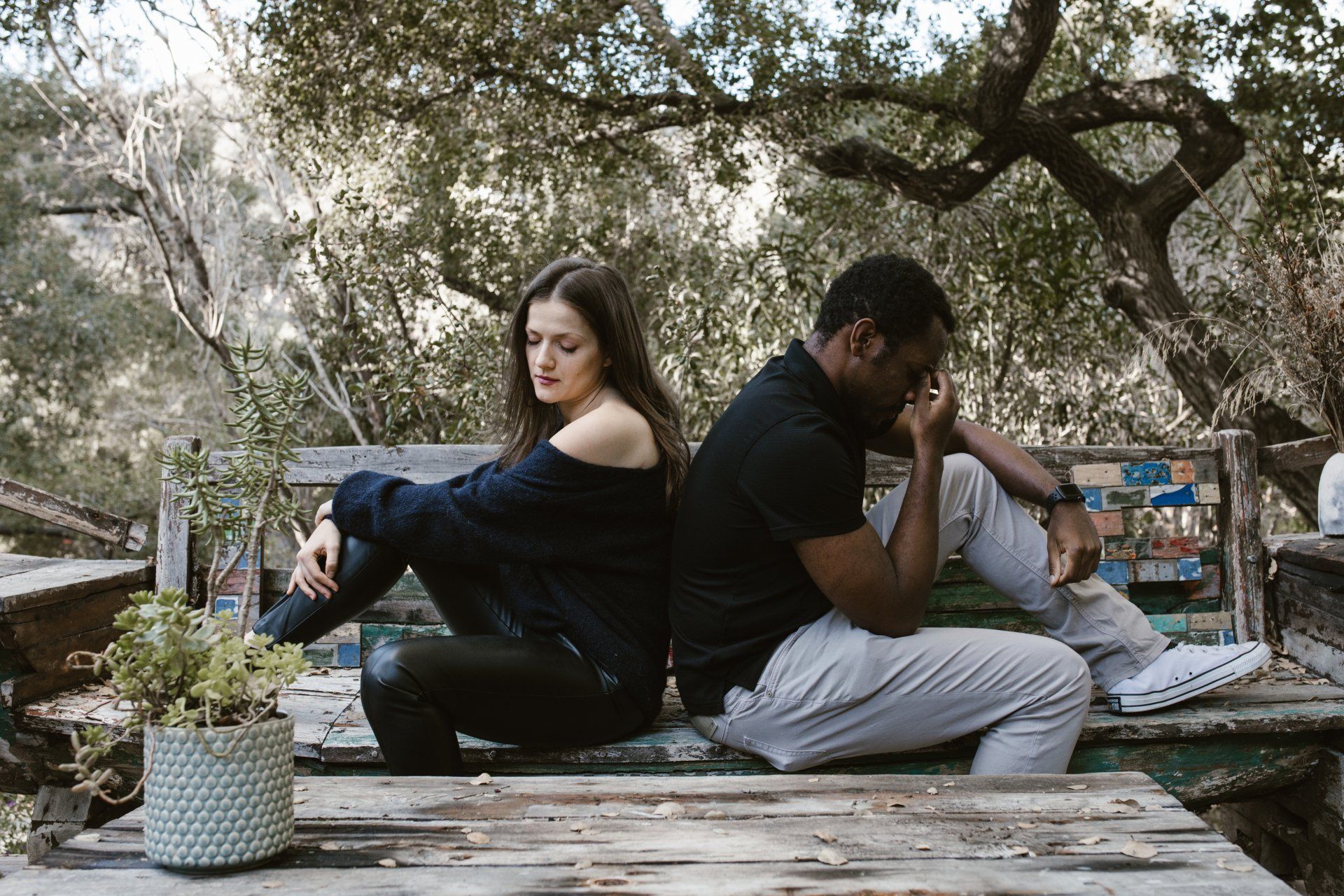 A man and a woman are sitting back to back on a bench.