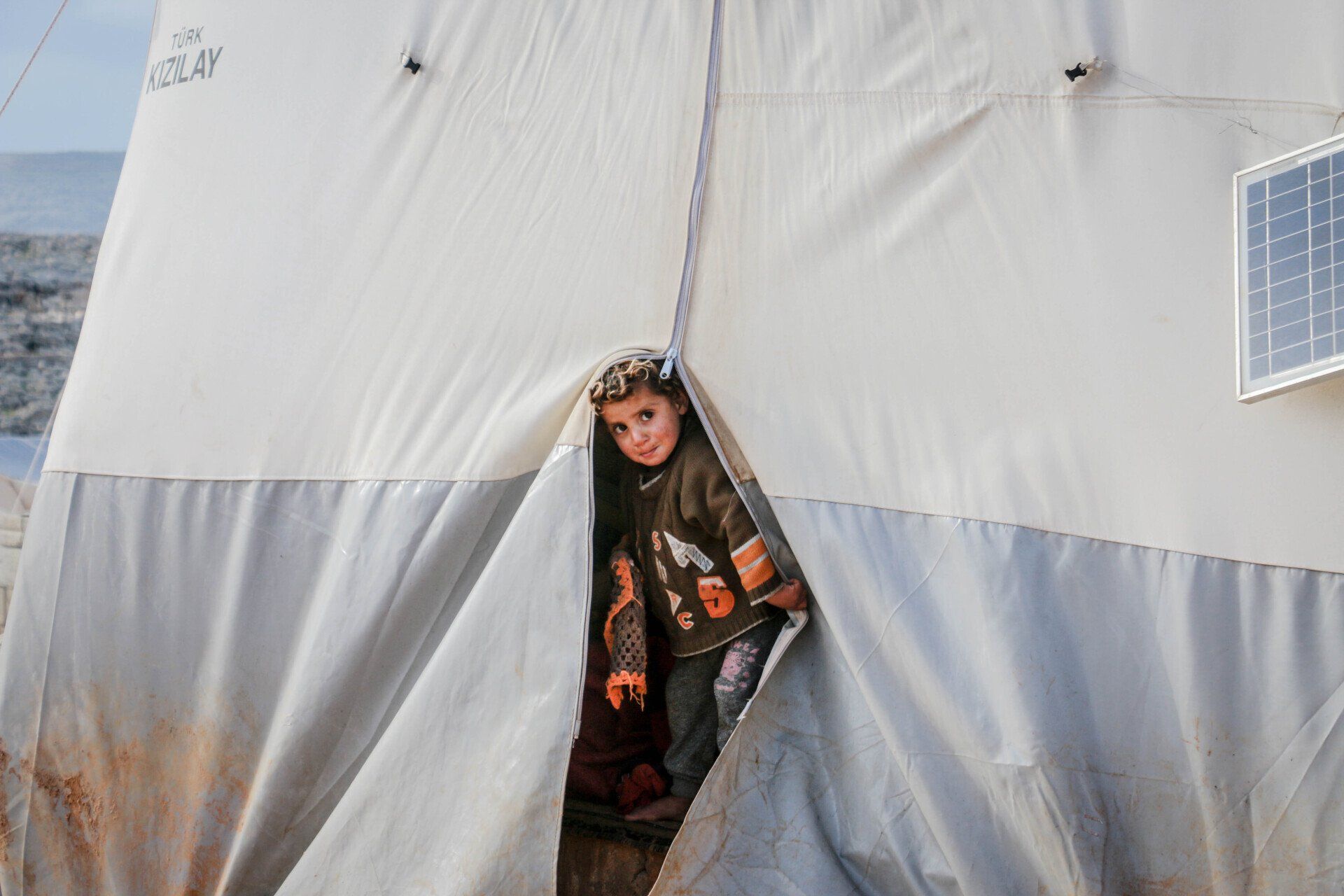 A boy is standing in a tent with a solar panel on the side.